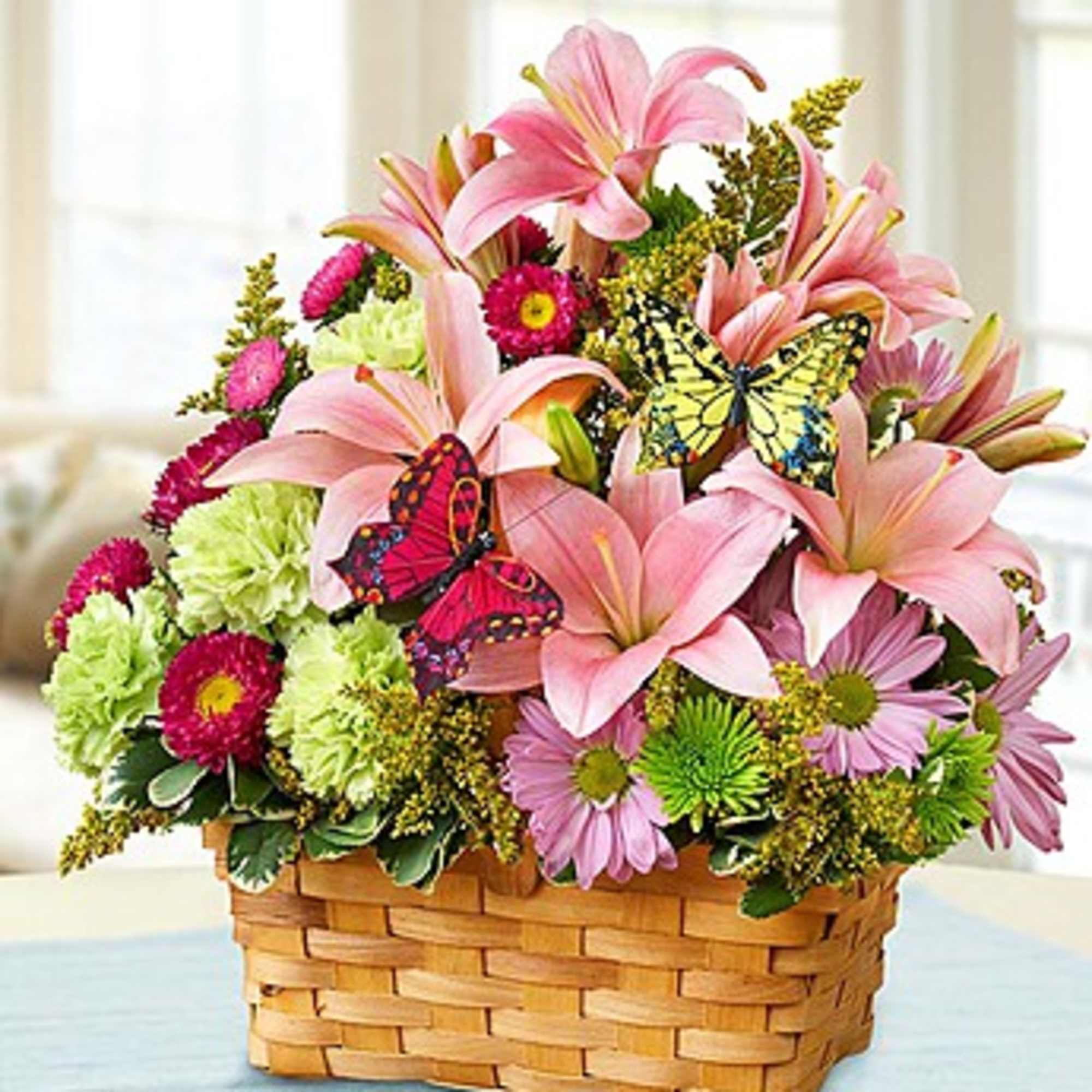 Basket arrangement of pink lilies and mixed daisies with butterfly picks