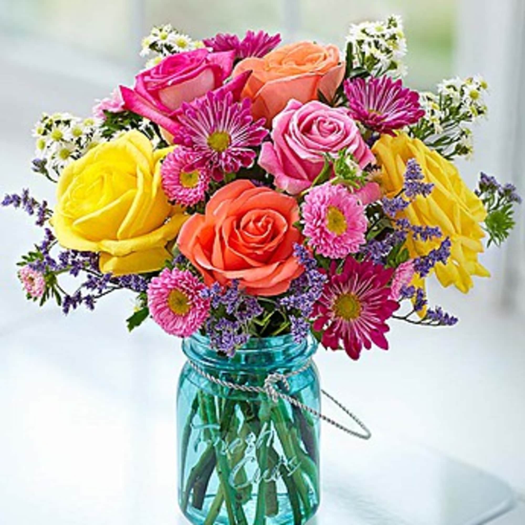 Colorful bouquet of roses and daisies in a blue glass jar