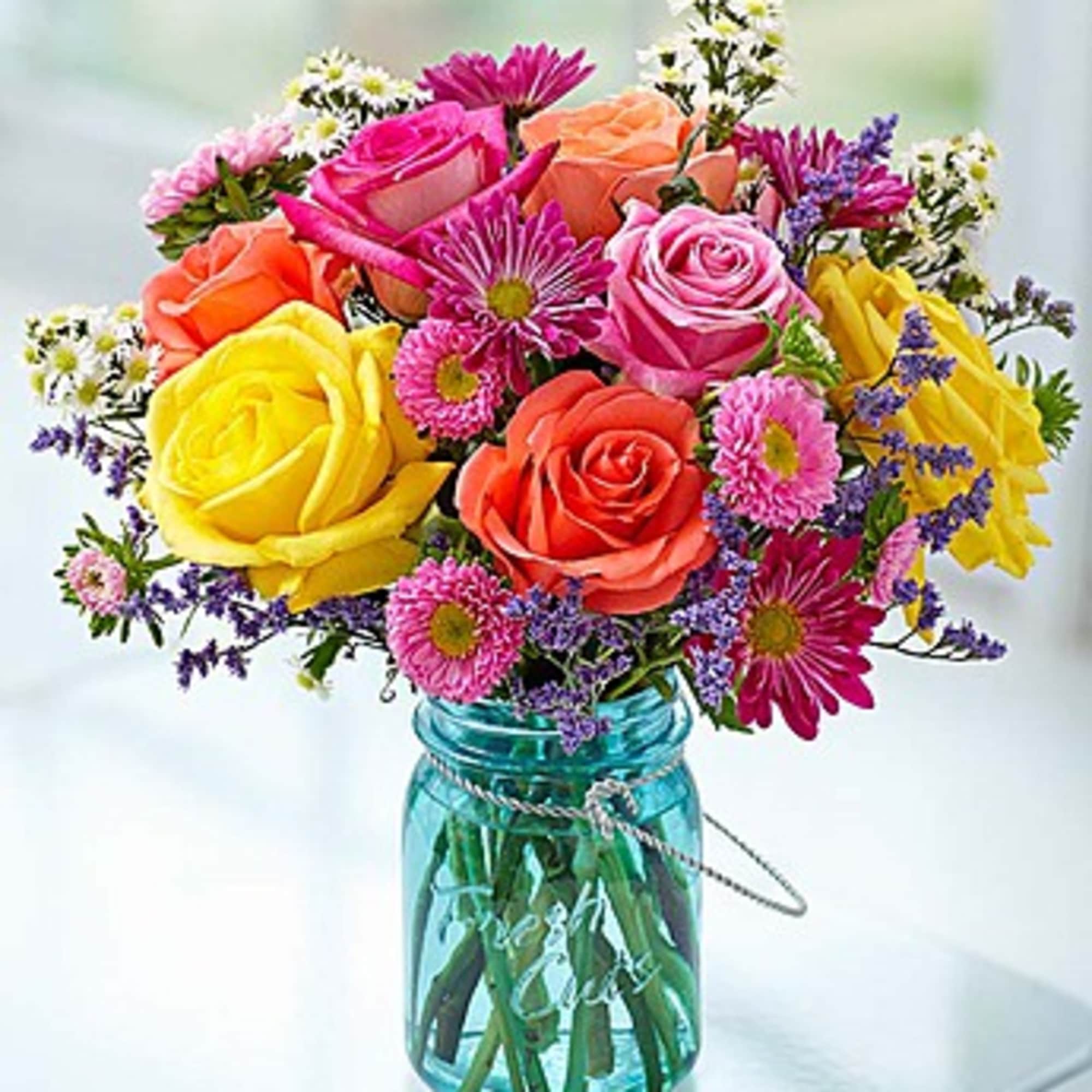 Colorful mixed bouquet of roses and daisies in a blue glass jar