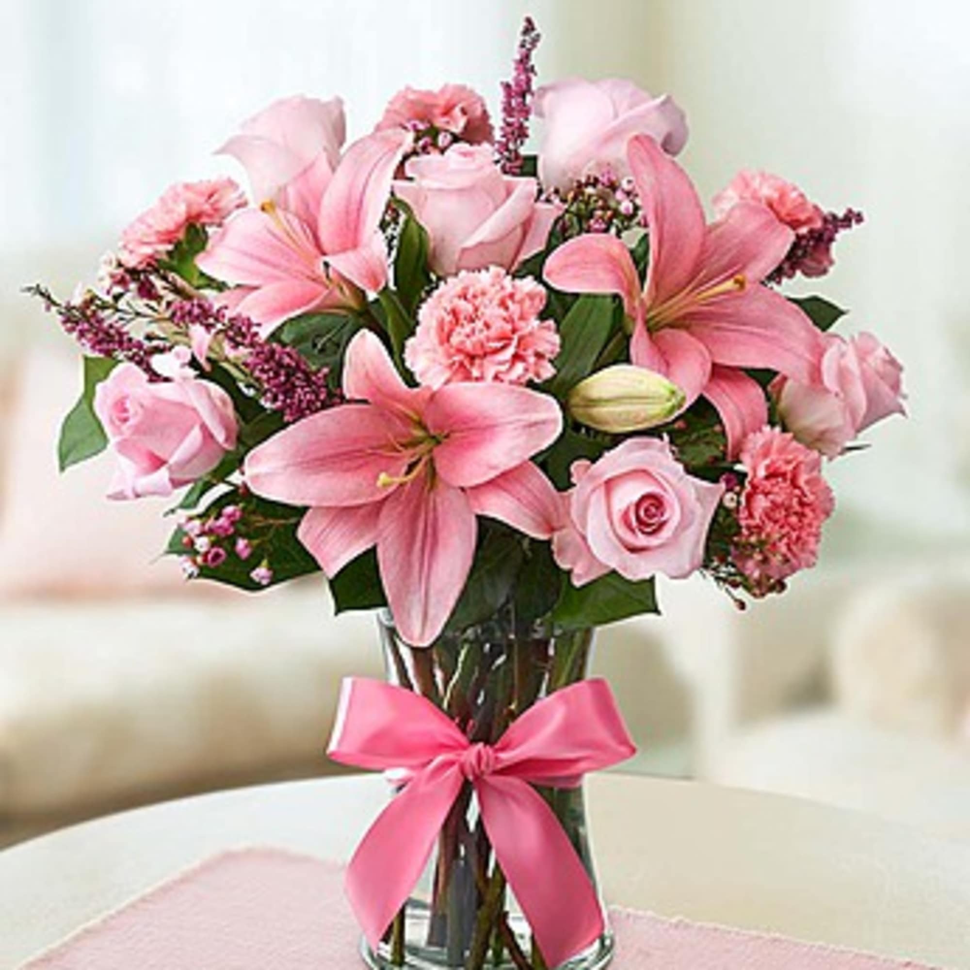 Pink lilies and roses arranged in a glass vase with a pink ribbon