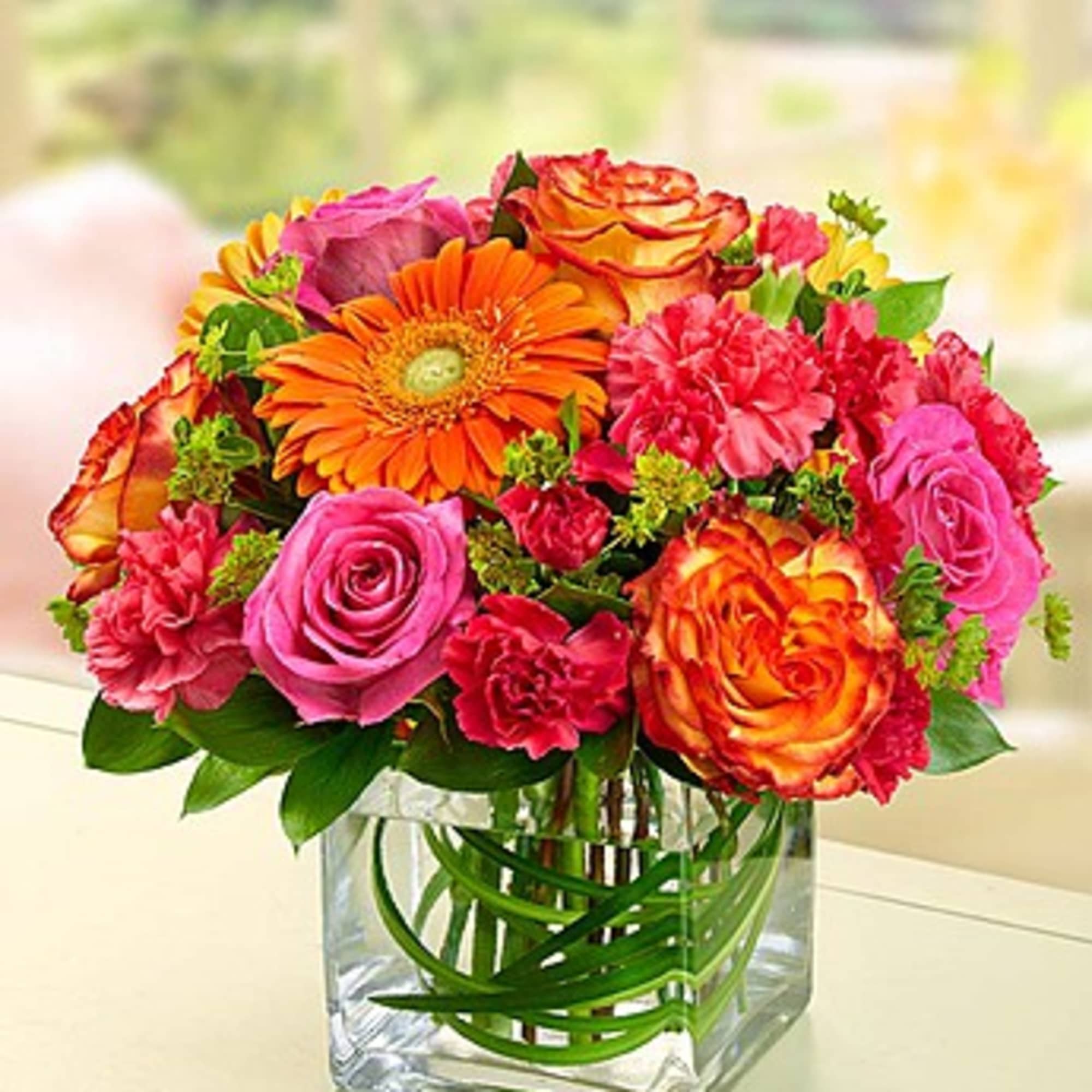 Mixed bouquet of pink, orange, and red flowers in a clear glass vase