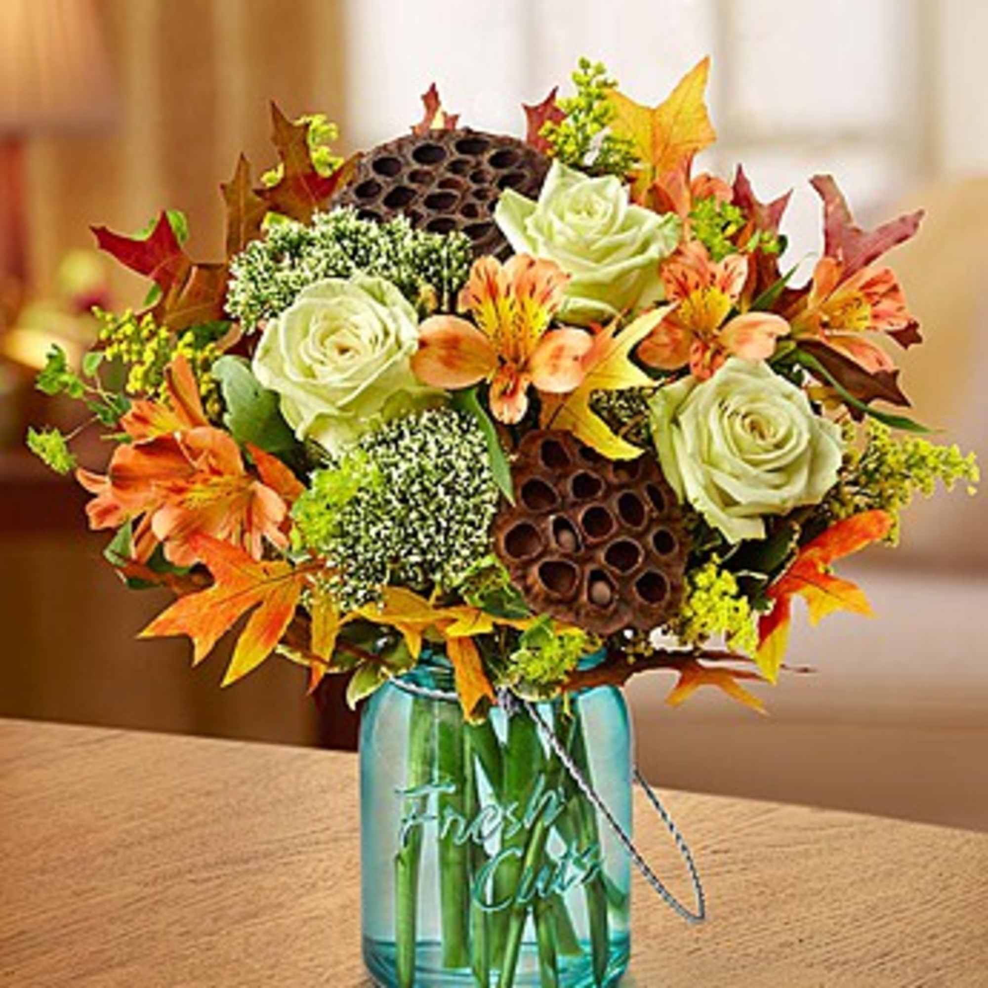 Autumn bouquet of roses and orange flowers in a blue glass vase
