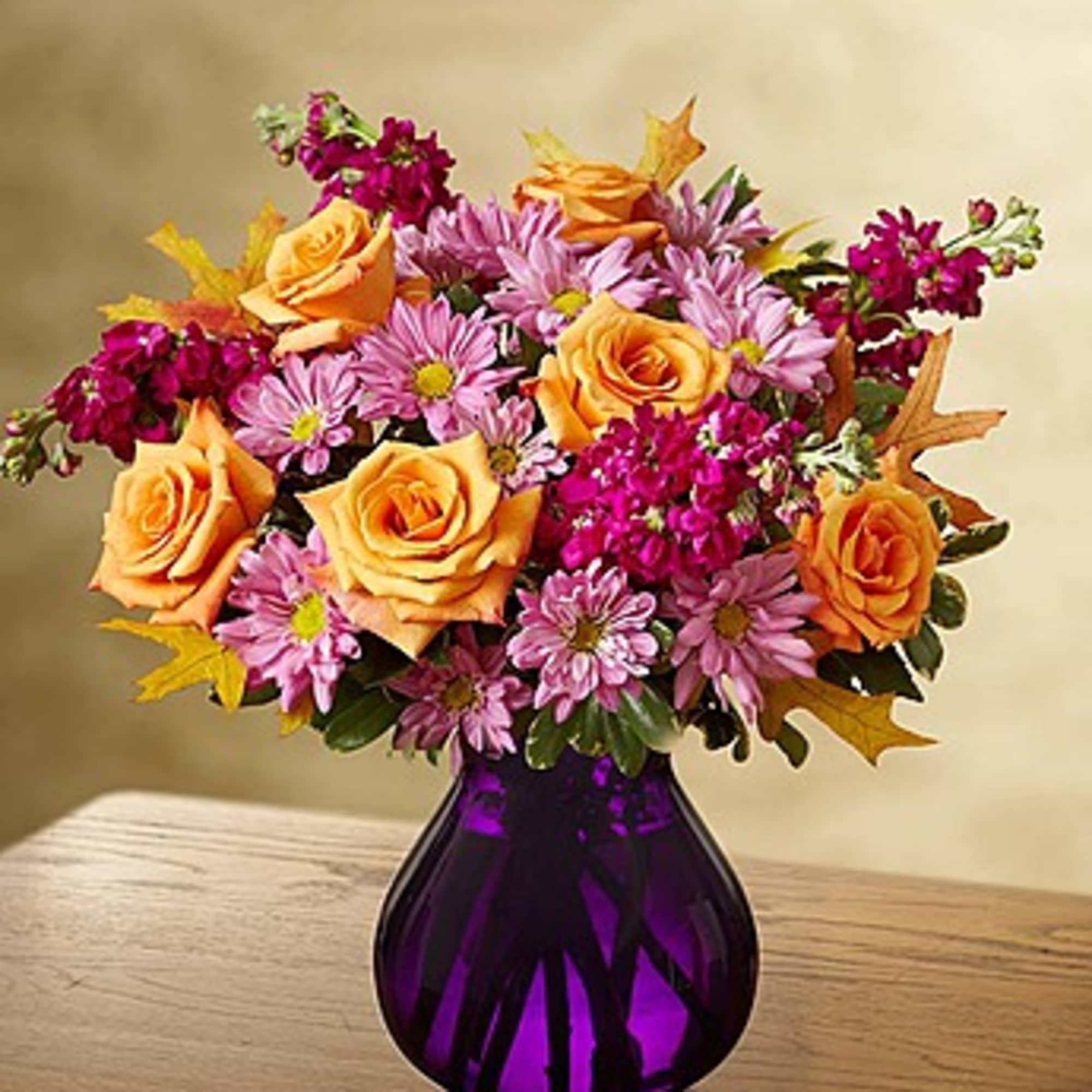 Orange roses and pink daisies in a purple vase