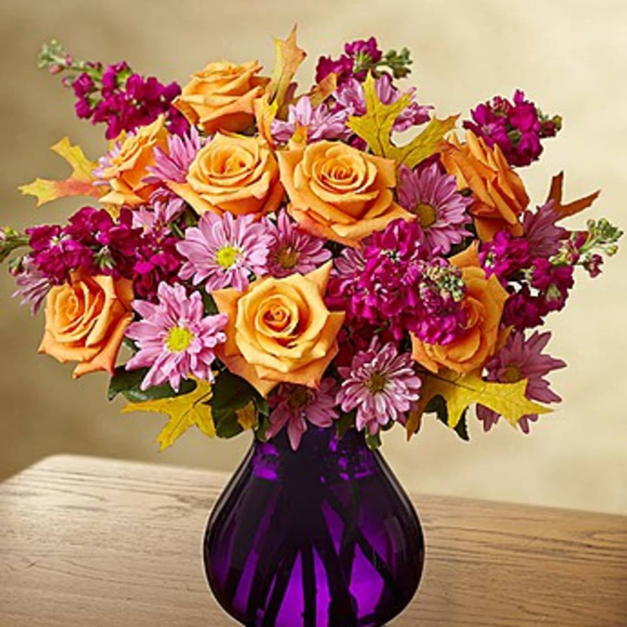 Bouquet of orange roses and purple daisies in a purple vase