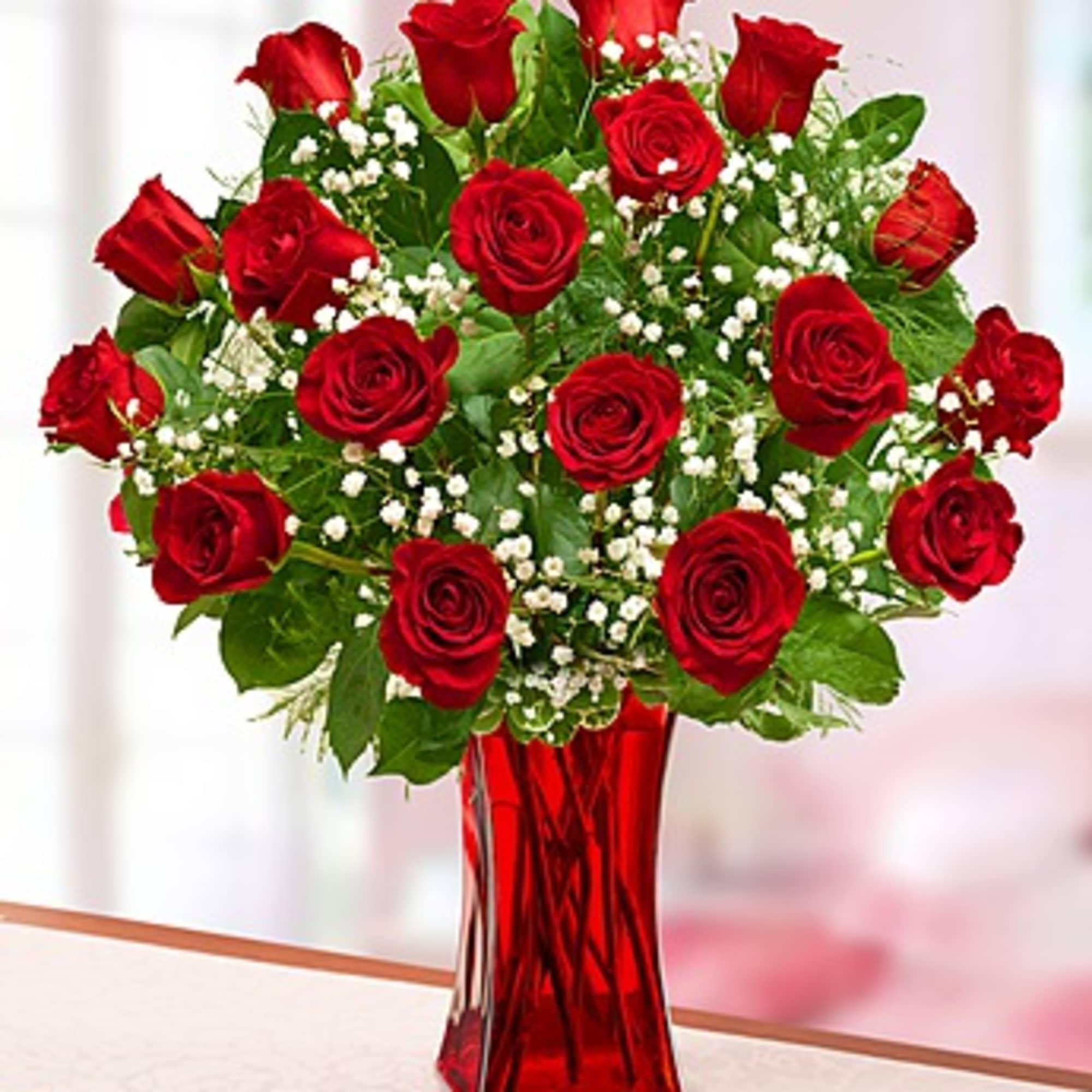 Red roses arranged in a tall red vase with white filler flowers