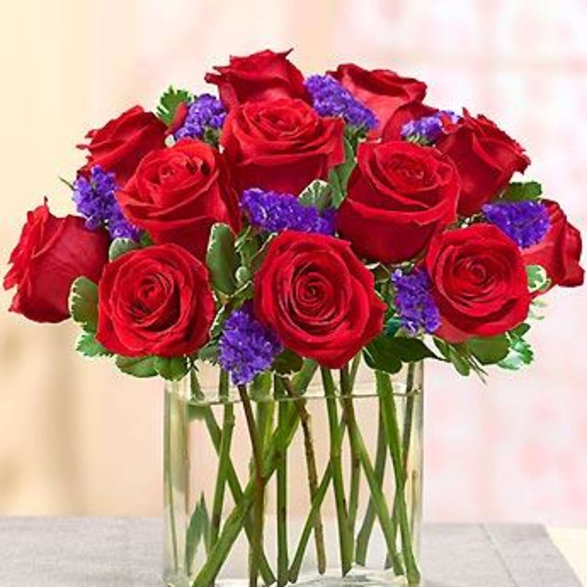 Red roses with purple filler in a clear glass vase