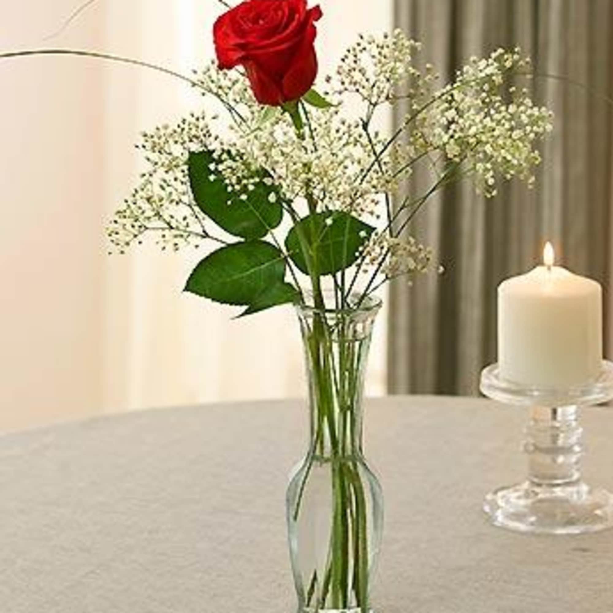 Single red rose in a glass vase with baby's breath and a lit candle