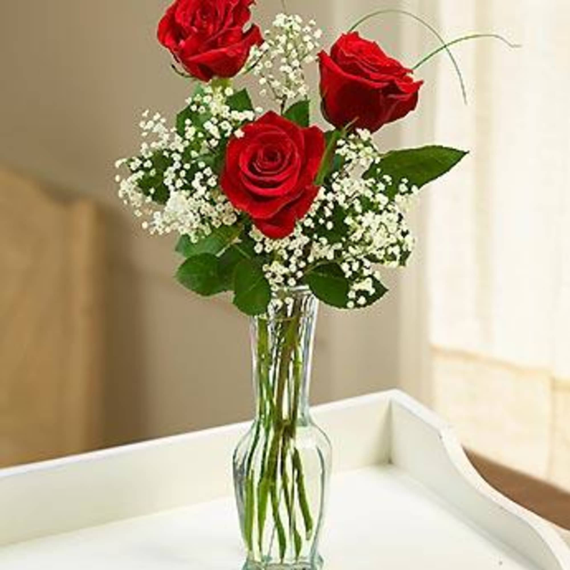 Three red roses in a clear glass vase with white baby's breath