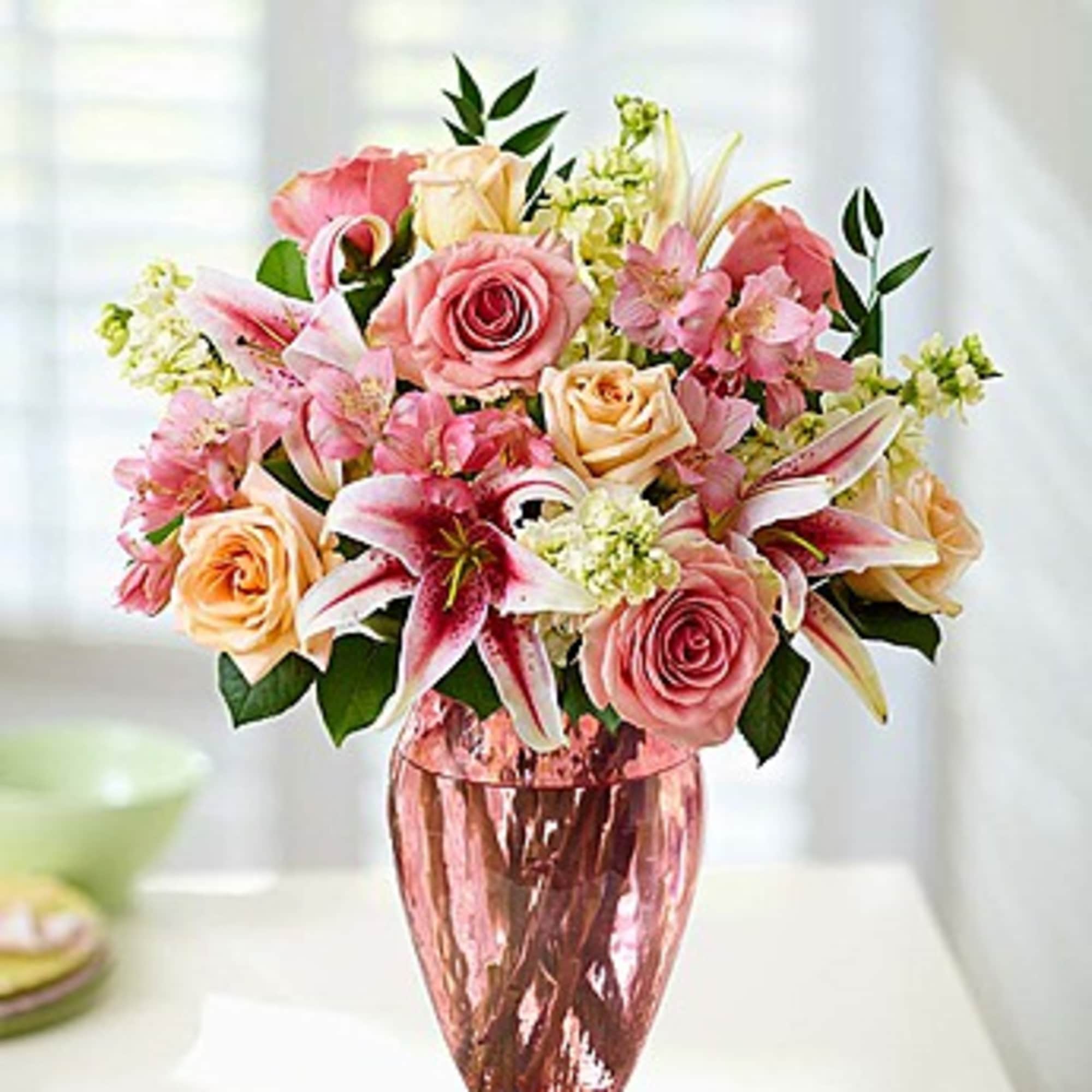 Pink and peach roses with lilies in a pink glass vase