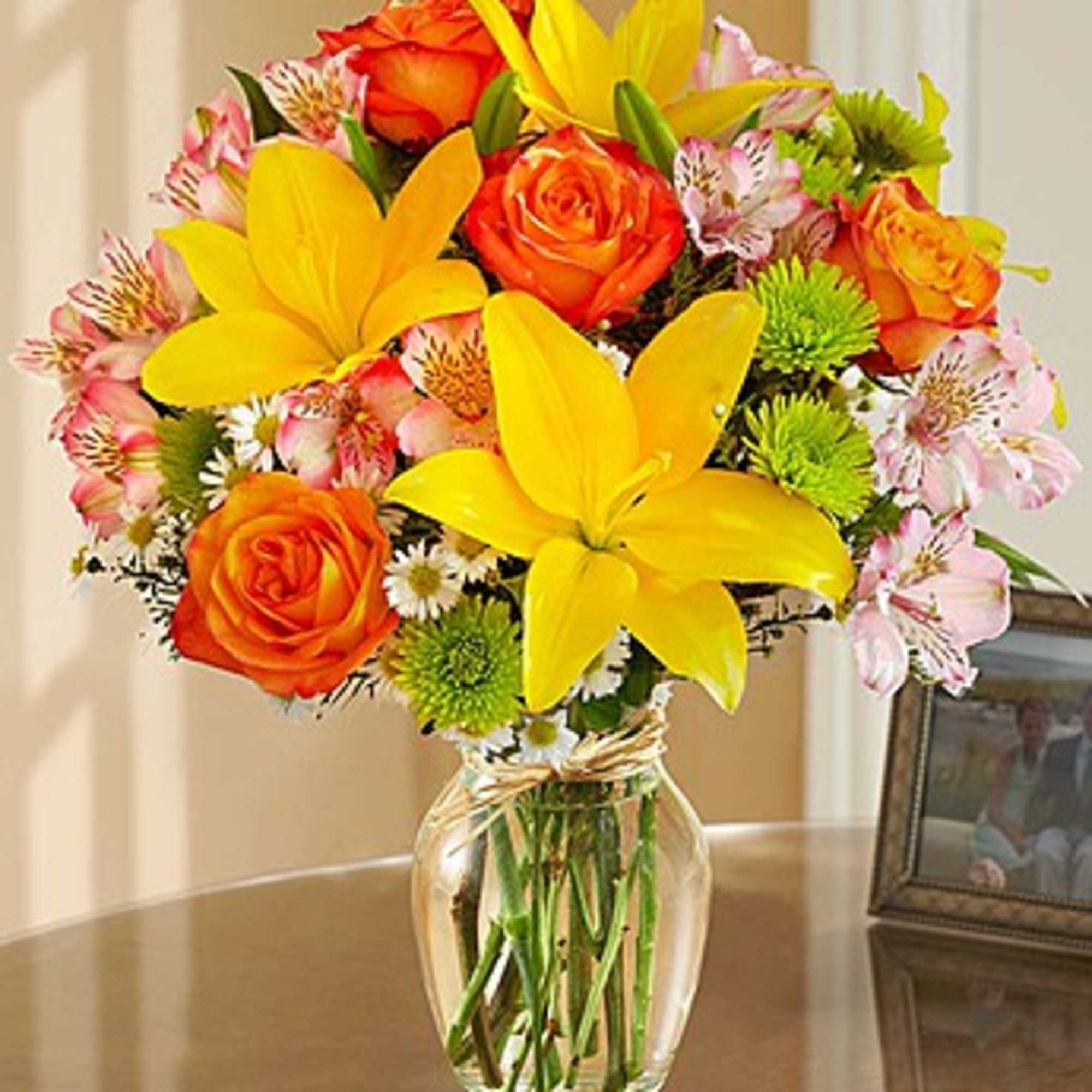 Bouquet of yellow lilies, orange roses, and pink alstroemeria in a glass vase, photo 3 of 3