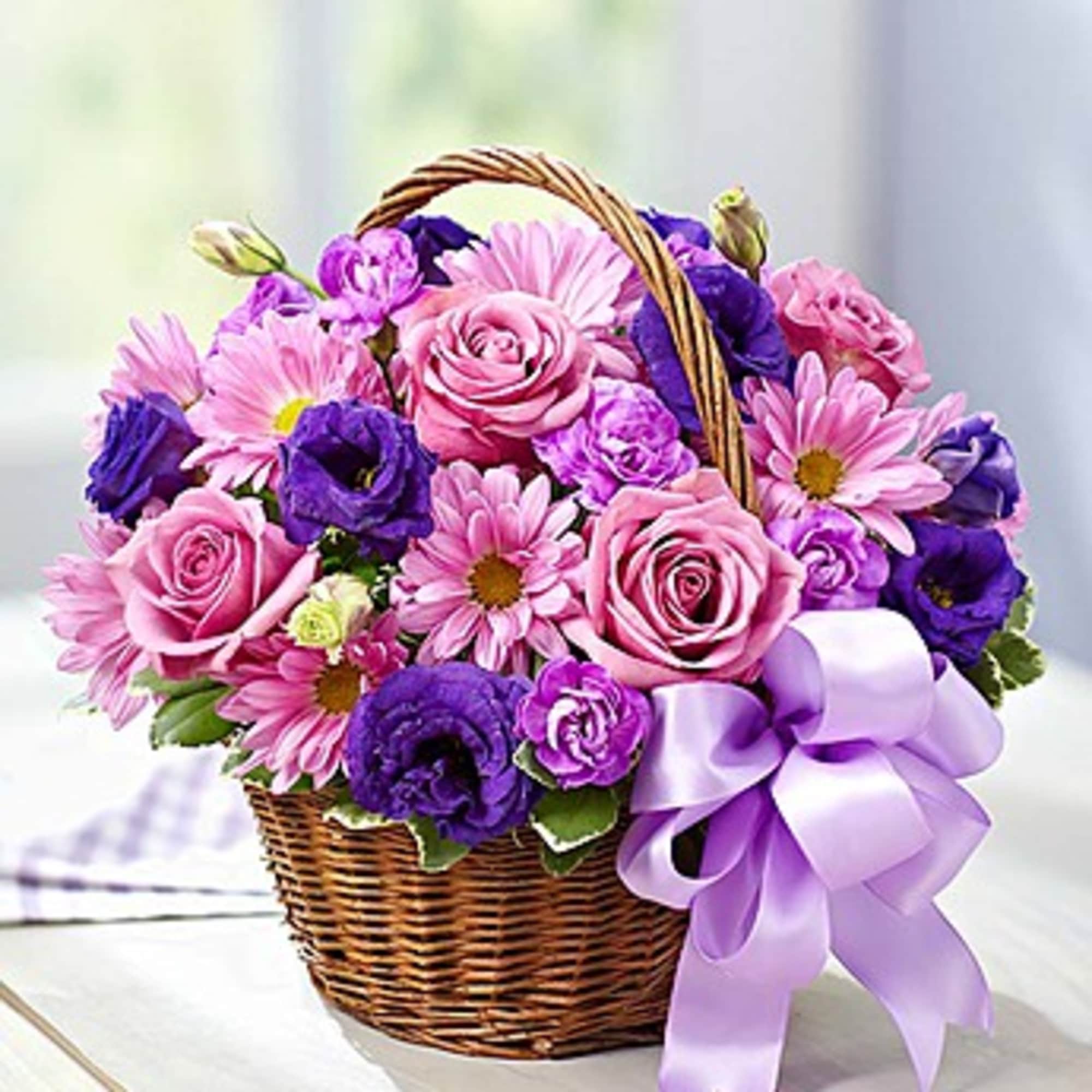 Pink and purple flowers arranged in a wicker basket with a lavender bow.