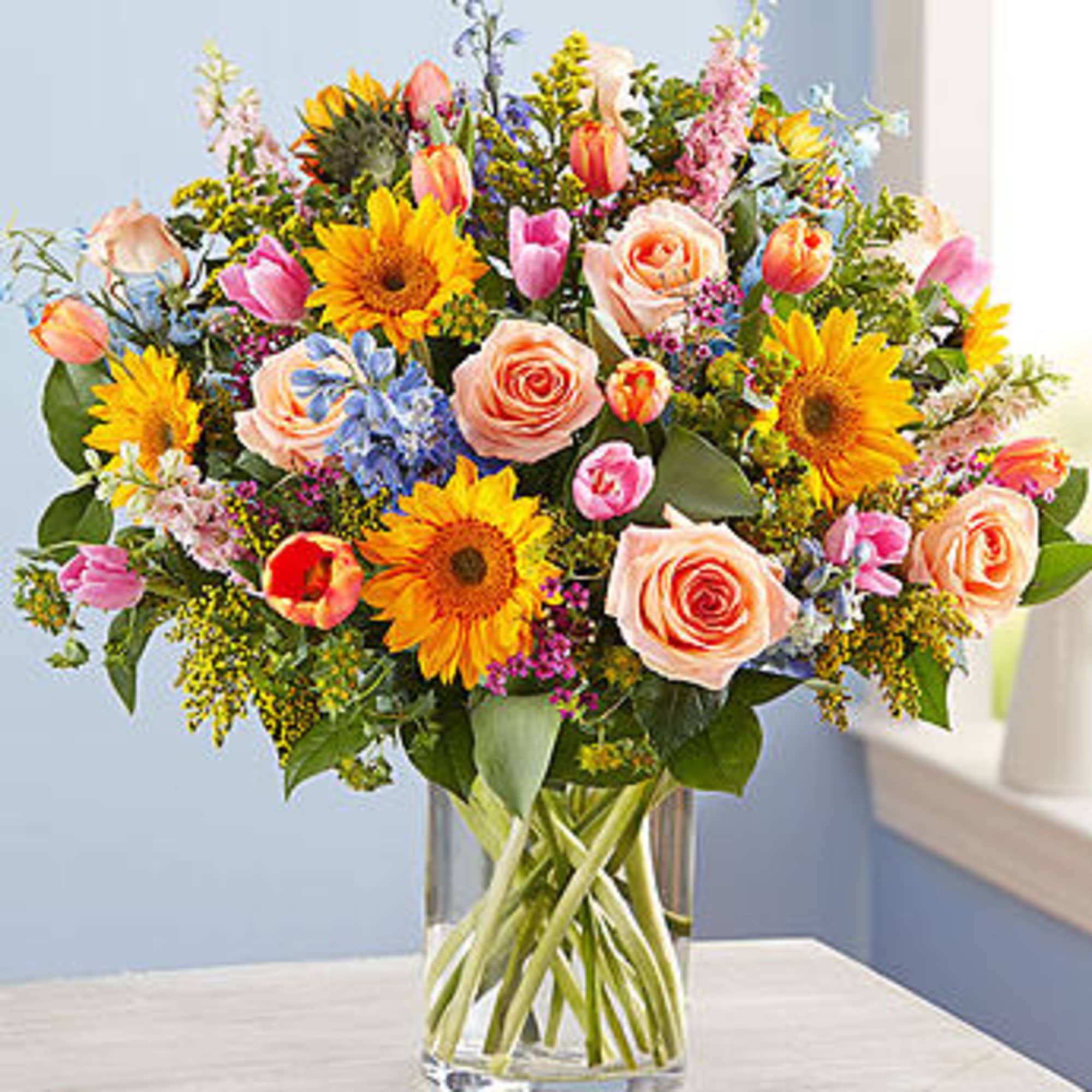 Mixed bouquet of sunflowers, roses, and tulips in a glass vase