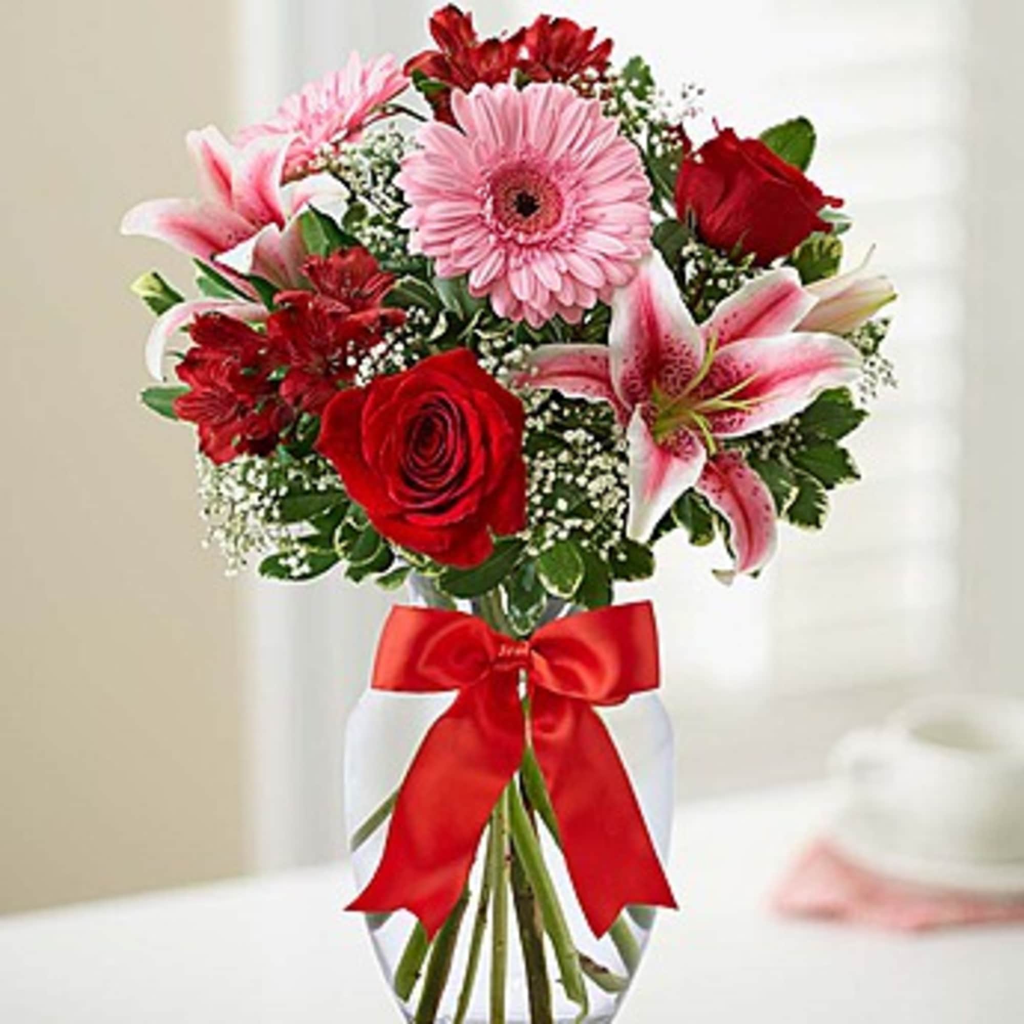 Bouquet of red and pink flowers in a clear glass vase with a red ribbon