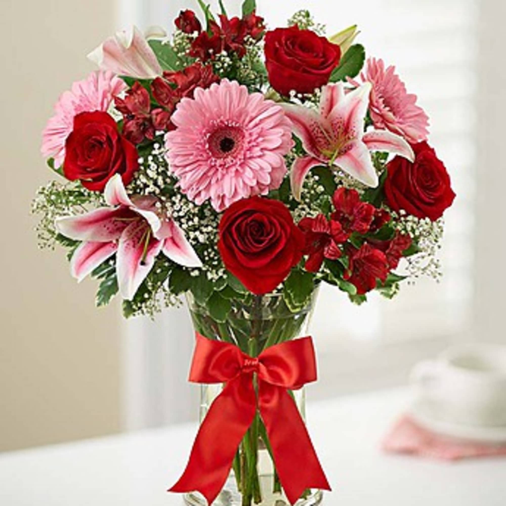 Bouquet of red roses, pink lilies, and a pink gerbera daisy in a glass vase