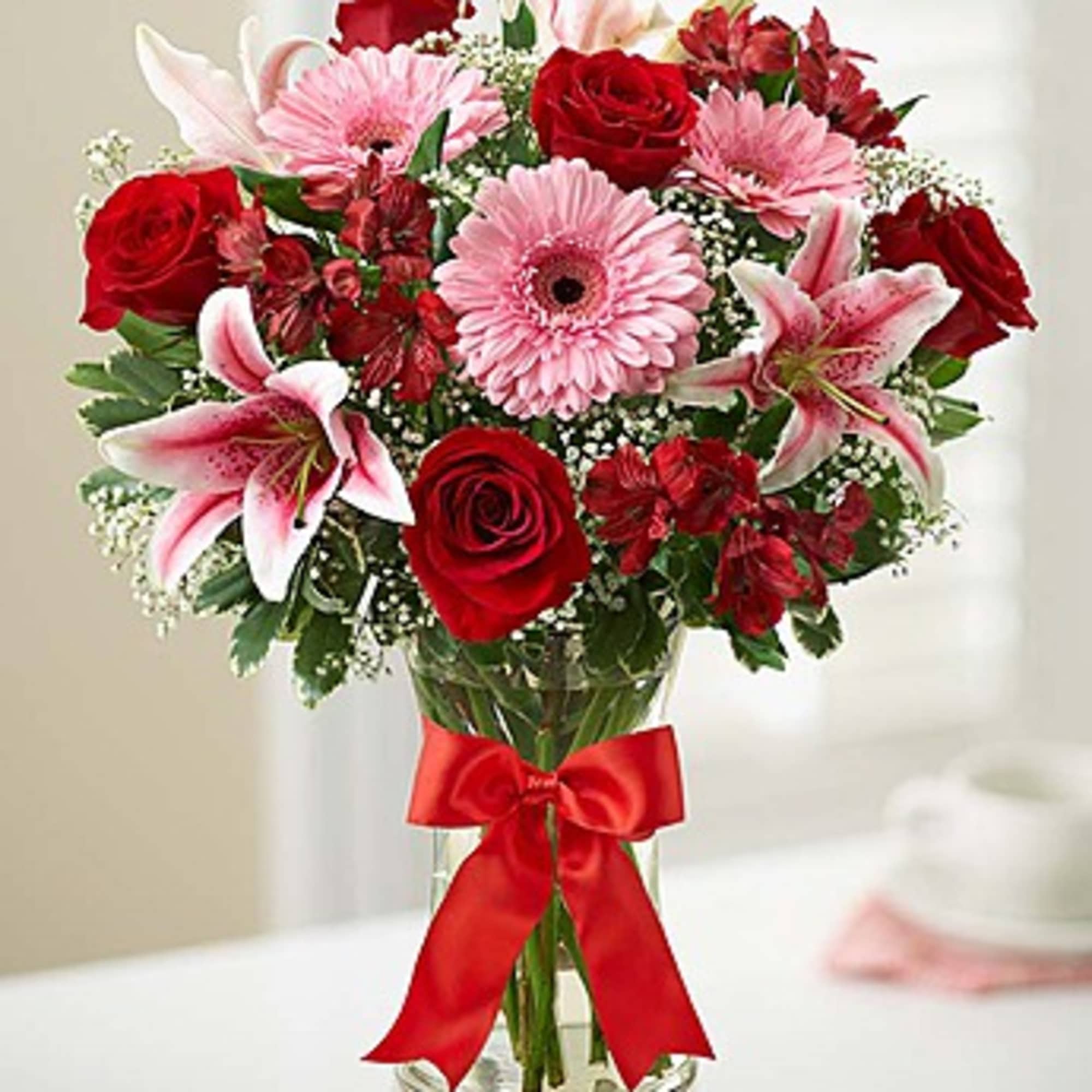 Red roses and pink lilies in a glass vase with a red ribbon