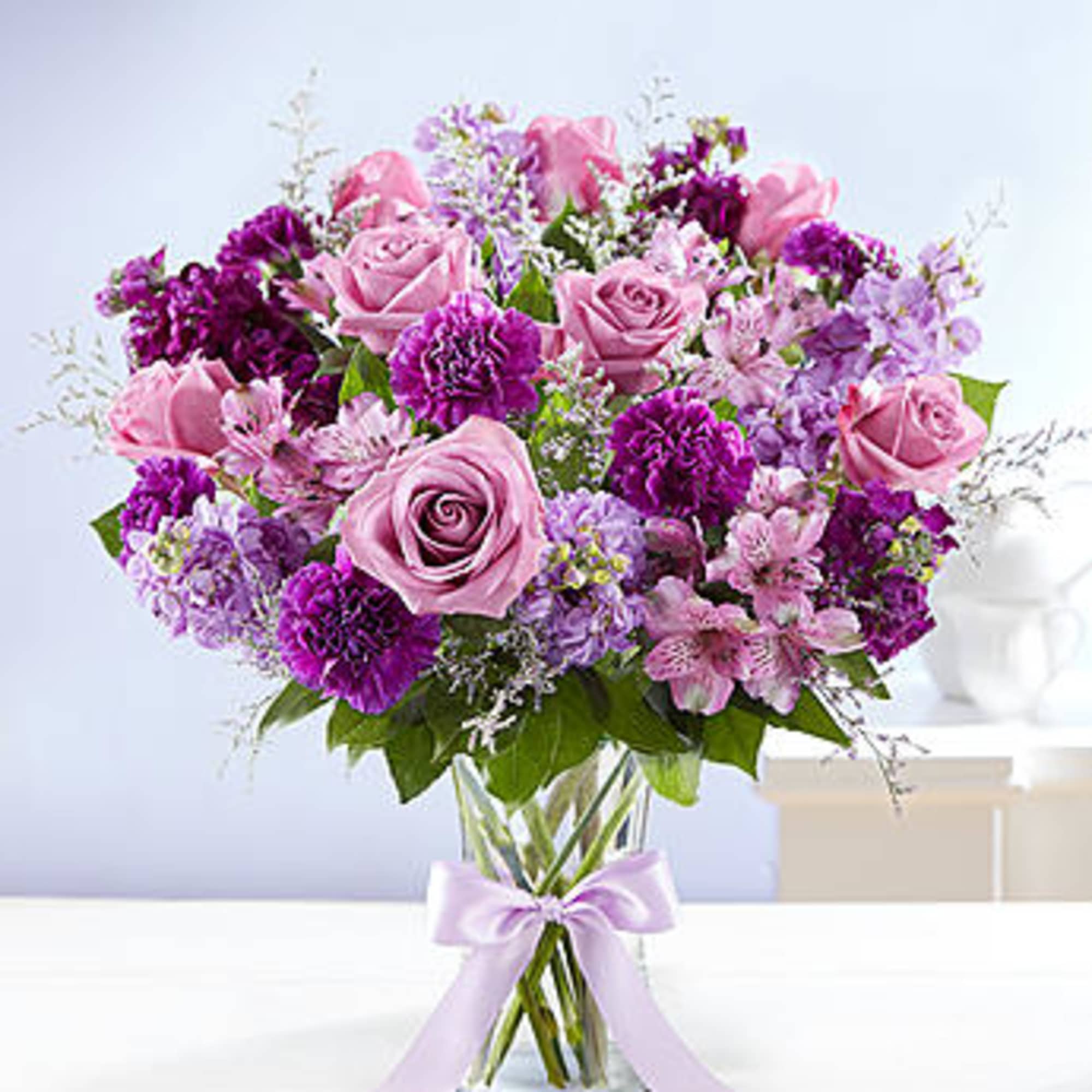 Pink and purple bouquet of roses and mixed flowers in a glass vase with a ribbon