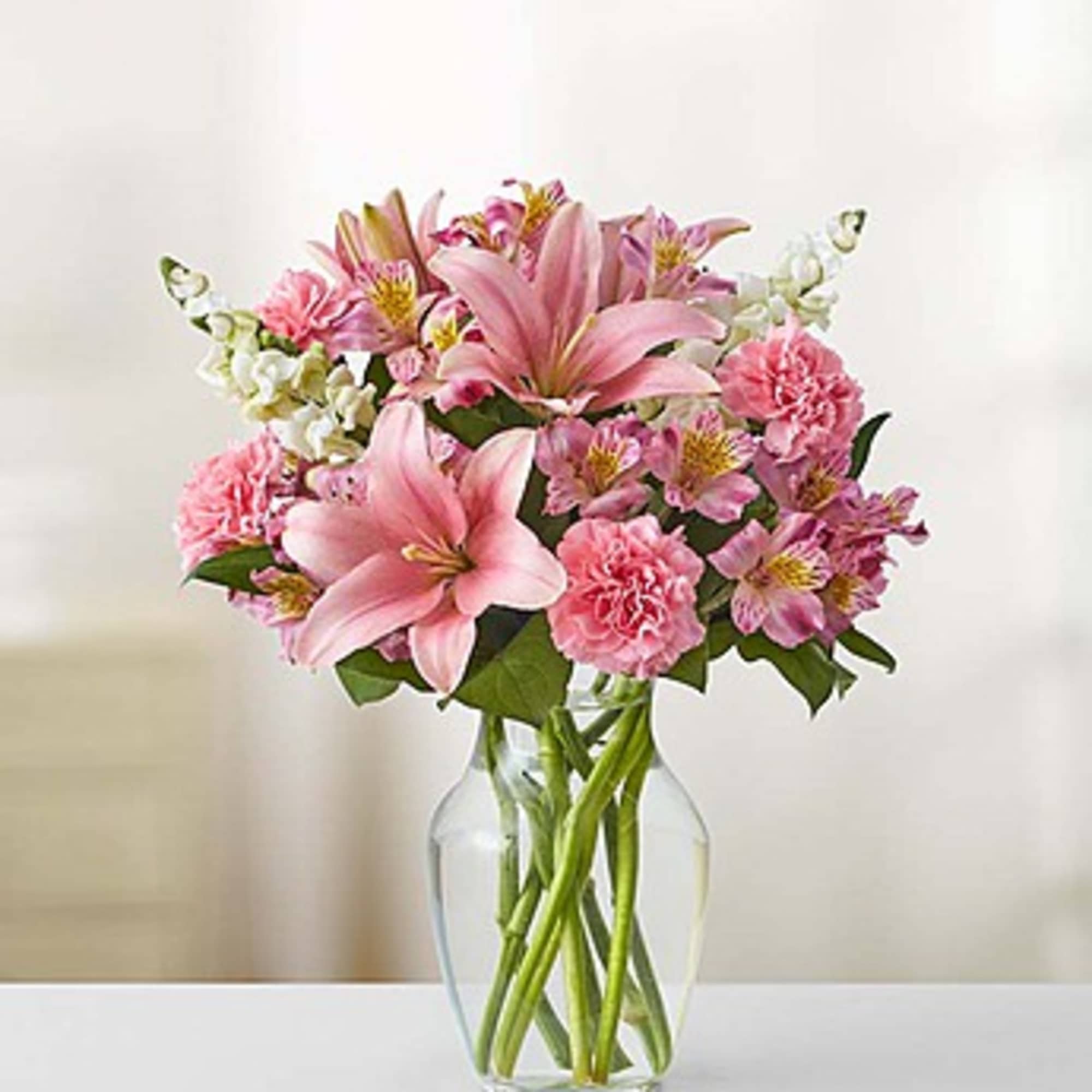 Pink lilies and carnations arranged in a clear glass vase