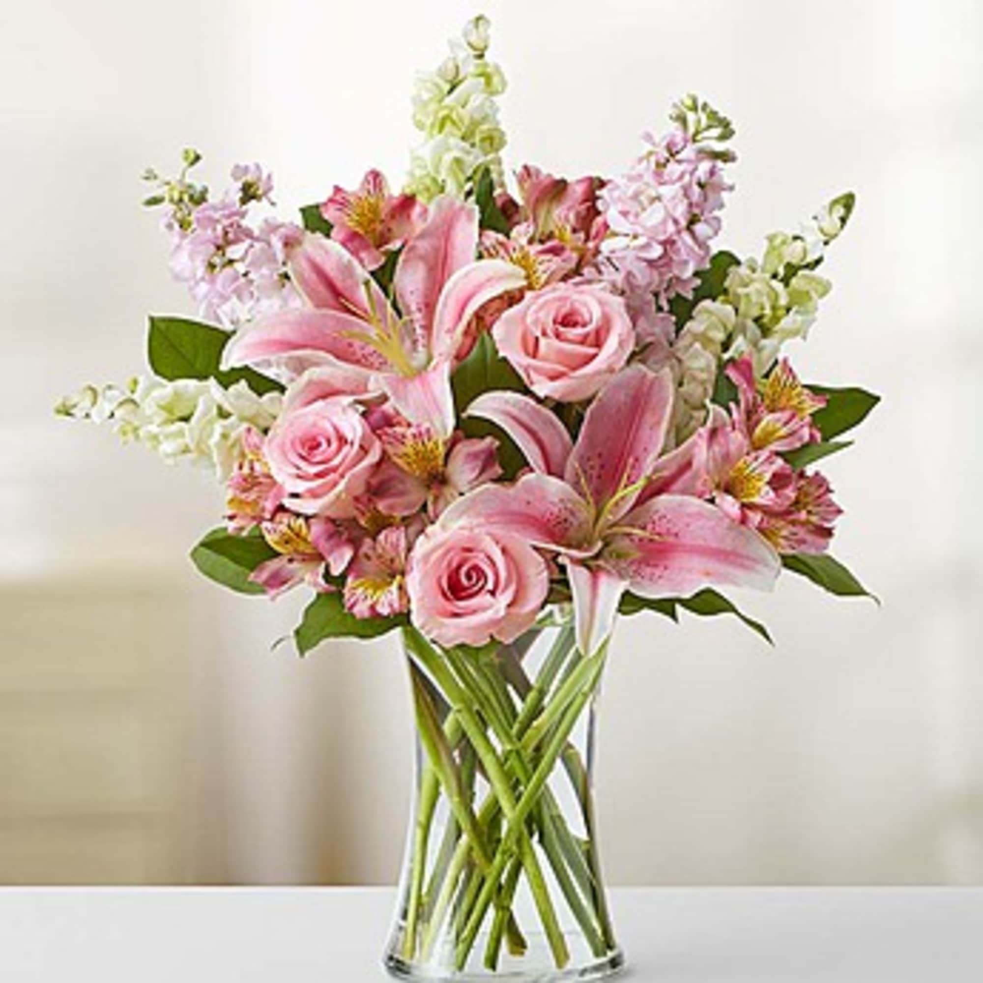 Pink lilies and roses arranged in a clear glass vase, photo 2 of 3