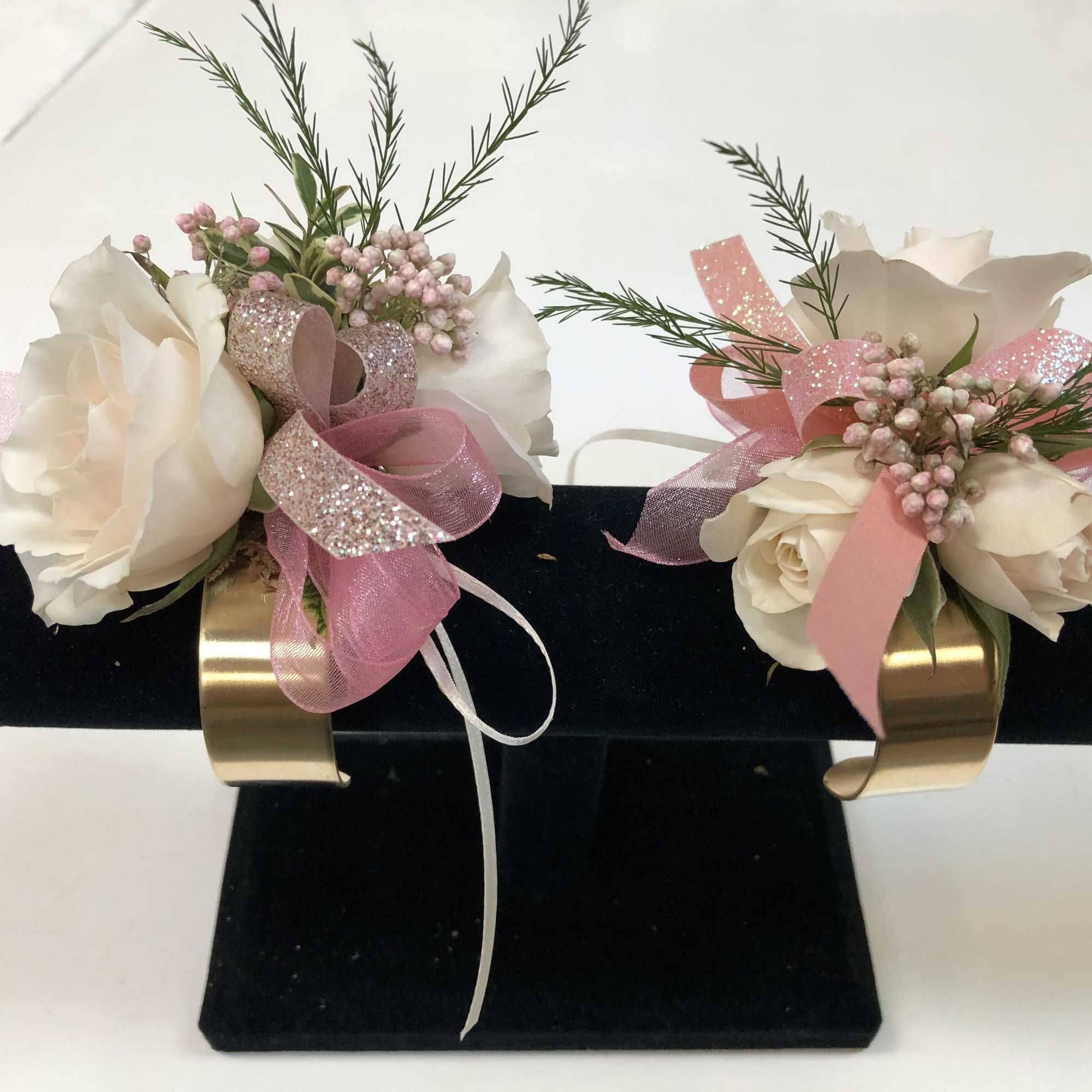 Pair of white floral corsages with pink ribbons on a black display stand