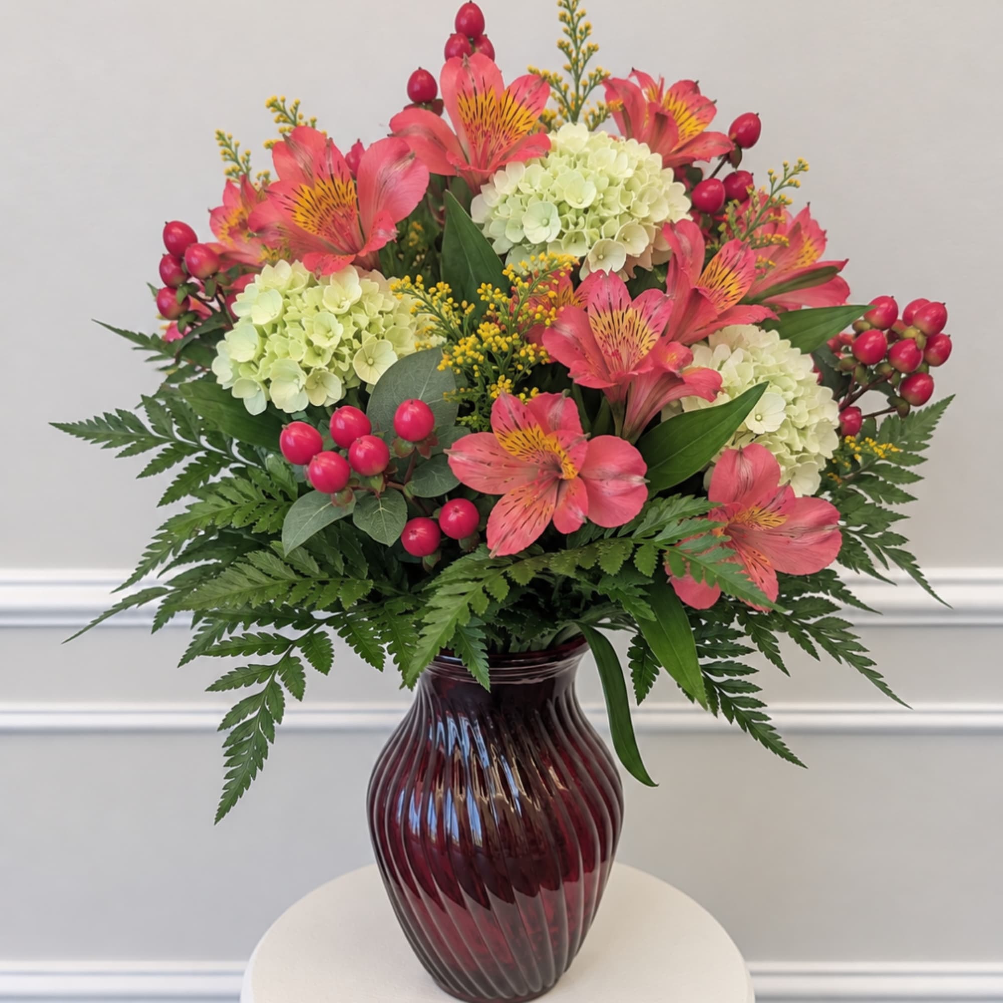 Pink alstroemeria and pale hydrangeas in a burgundy glass vase
