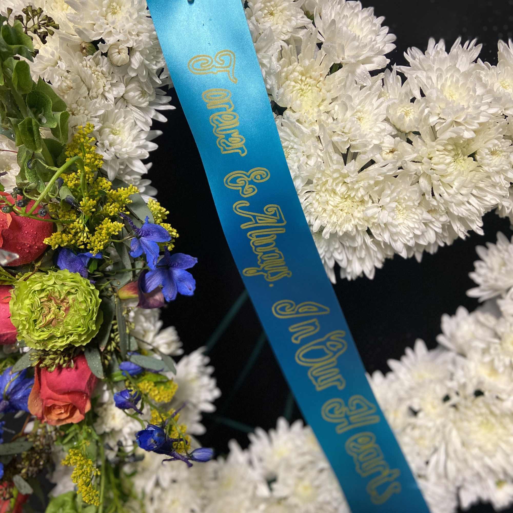 White chrysanthemum wreath with a blue memorial ribbon and mixed flowers