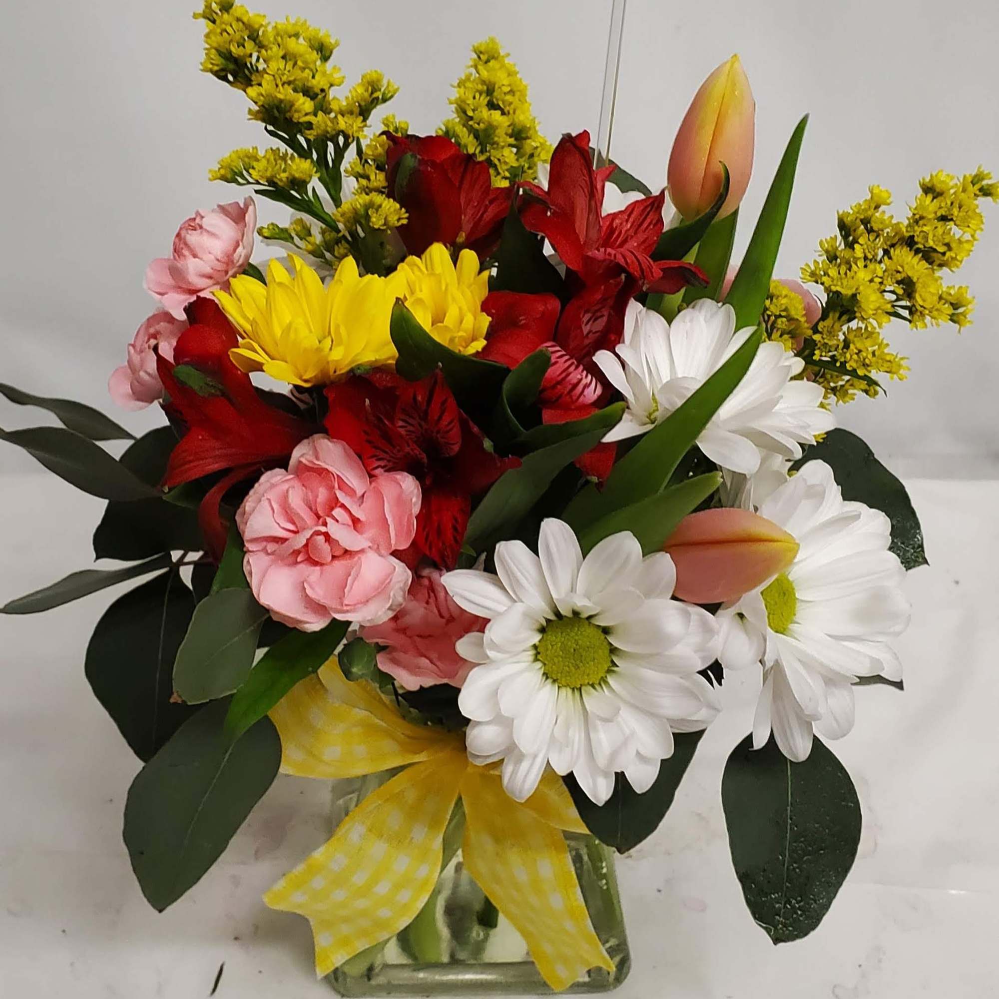 Mixed bouquet in a glass vase with daisies, tulips, carnations, and red blooms
