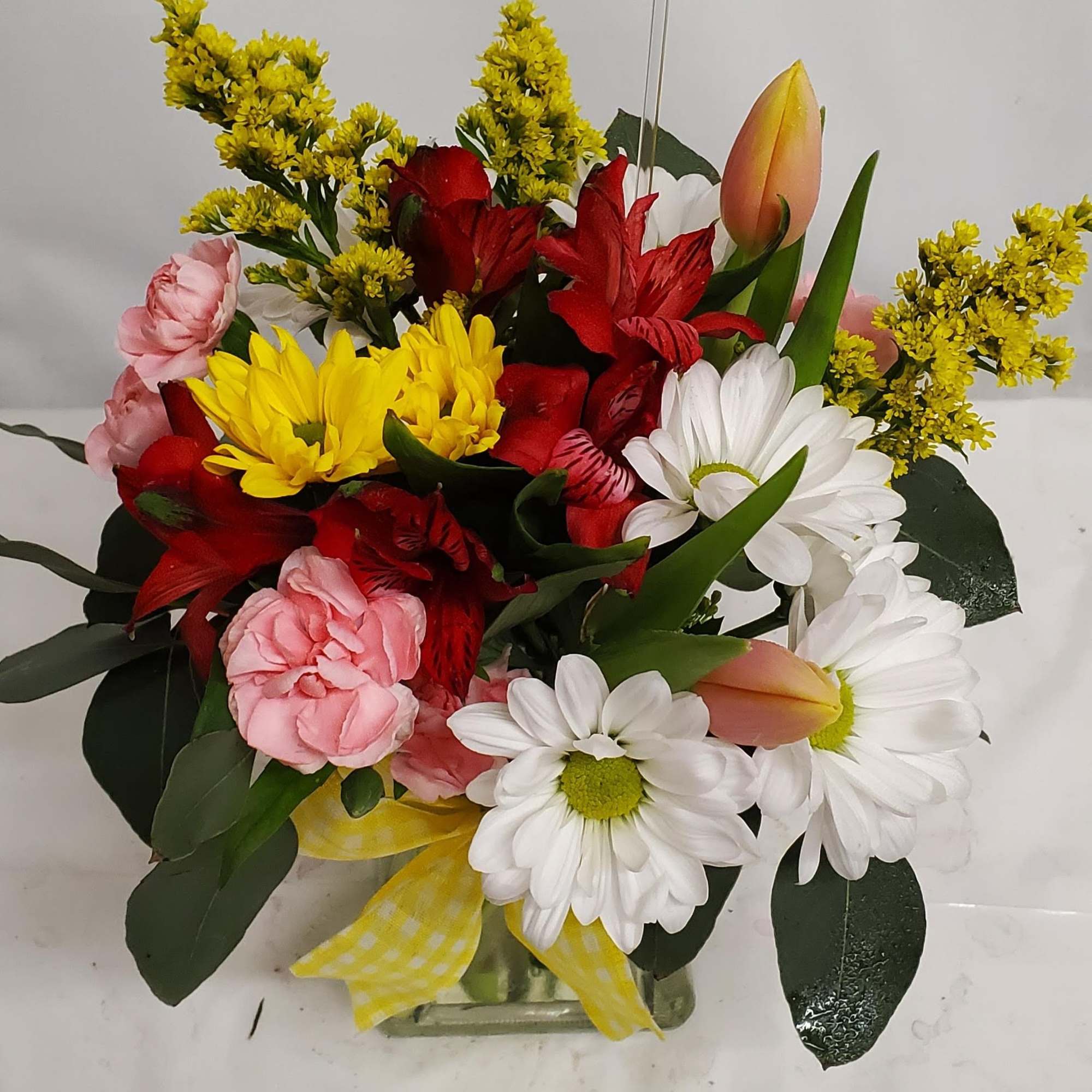Mixed bouquet of daisies, tulips, and red blooms in a glass vase