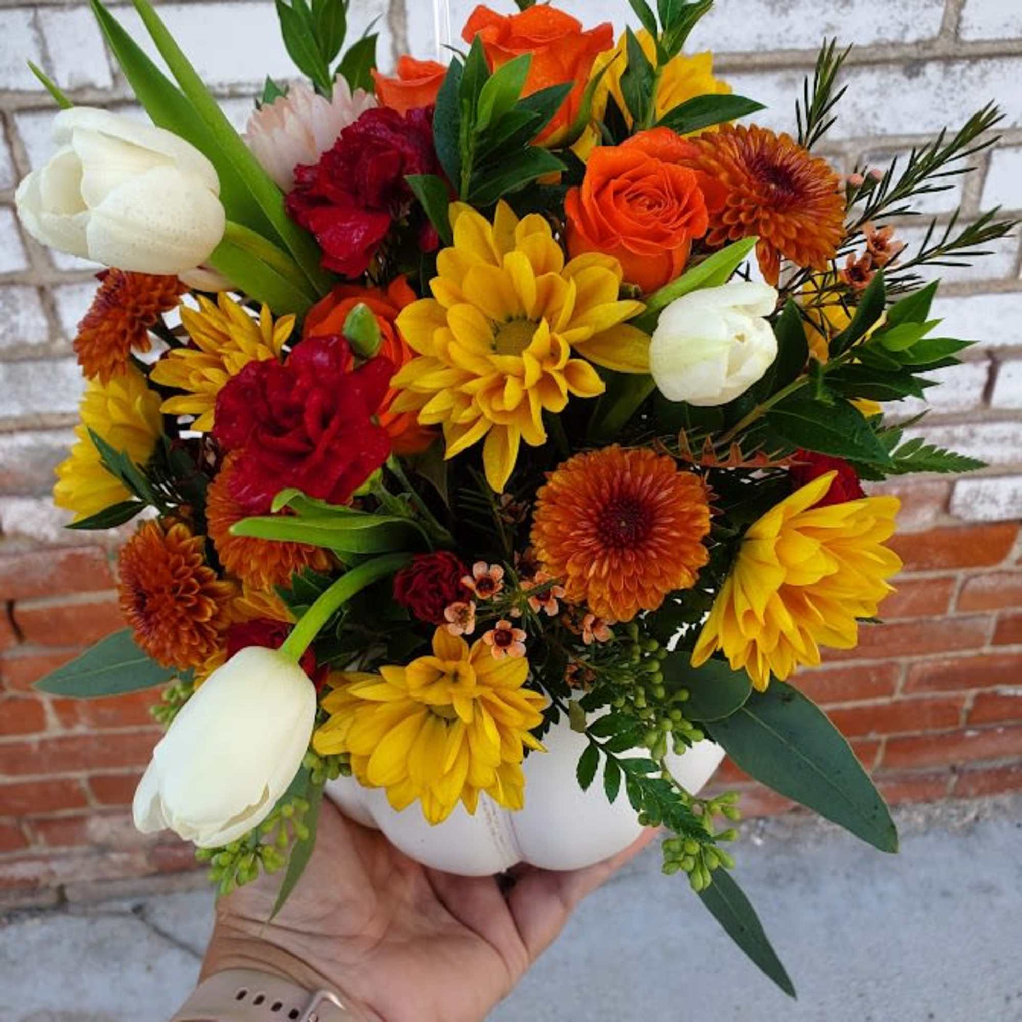 Mixed bouquet of orange, yellow, red, and white flowers in a white vase