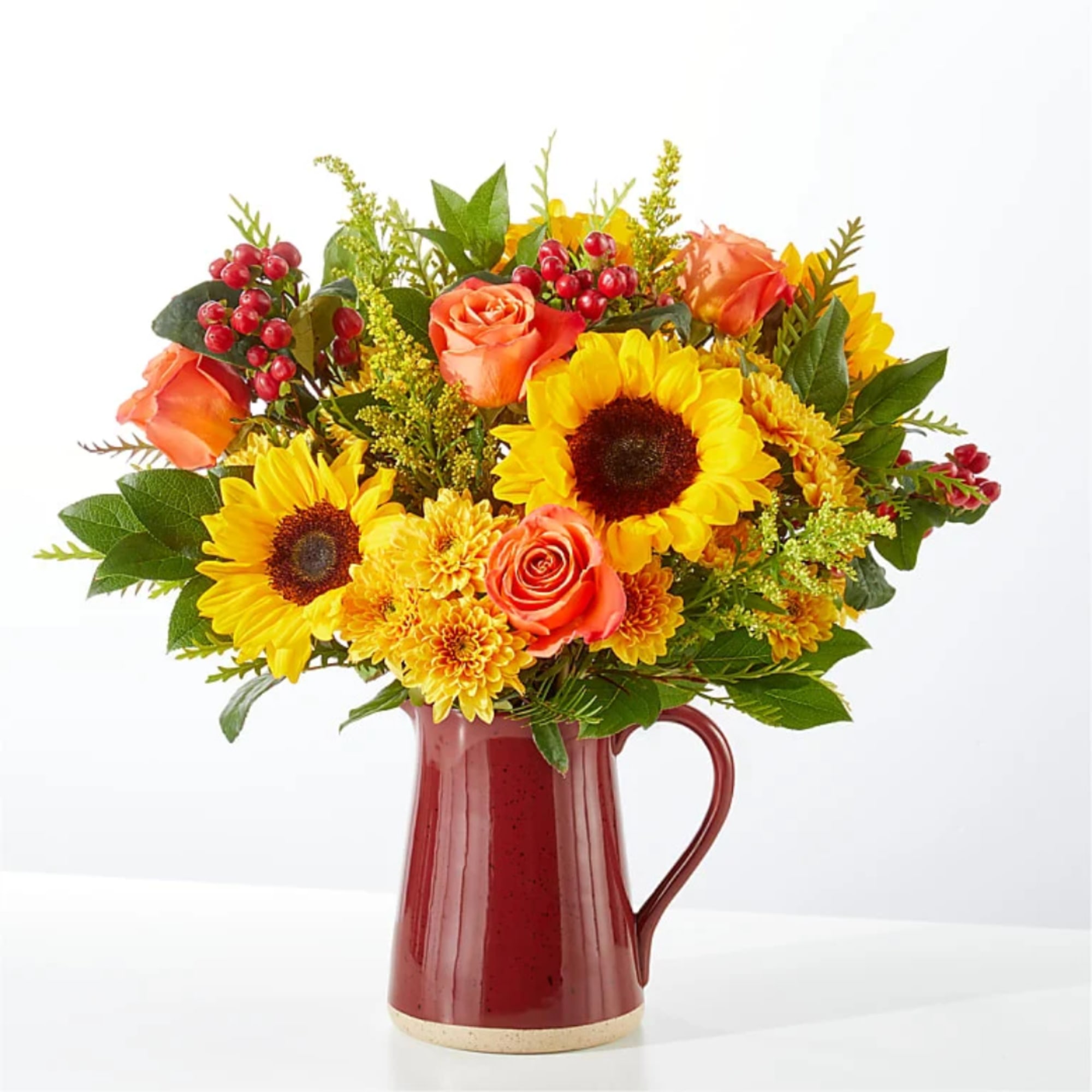 Bouquet of sunflowers, orange roses, and yellow mums in a red pitcher vase