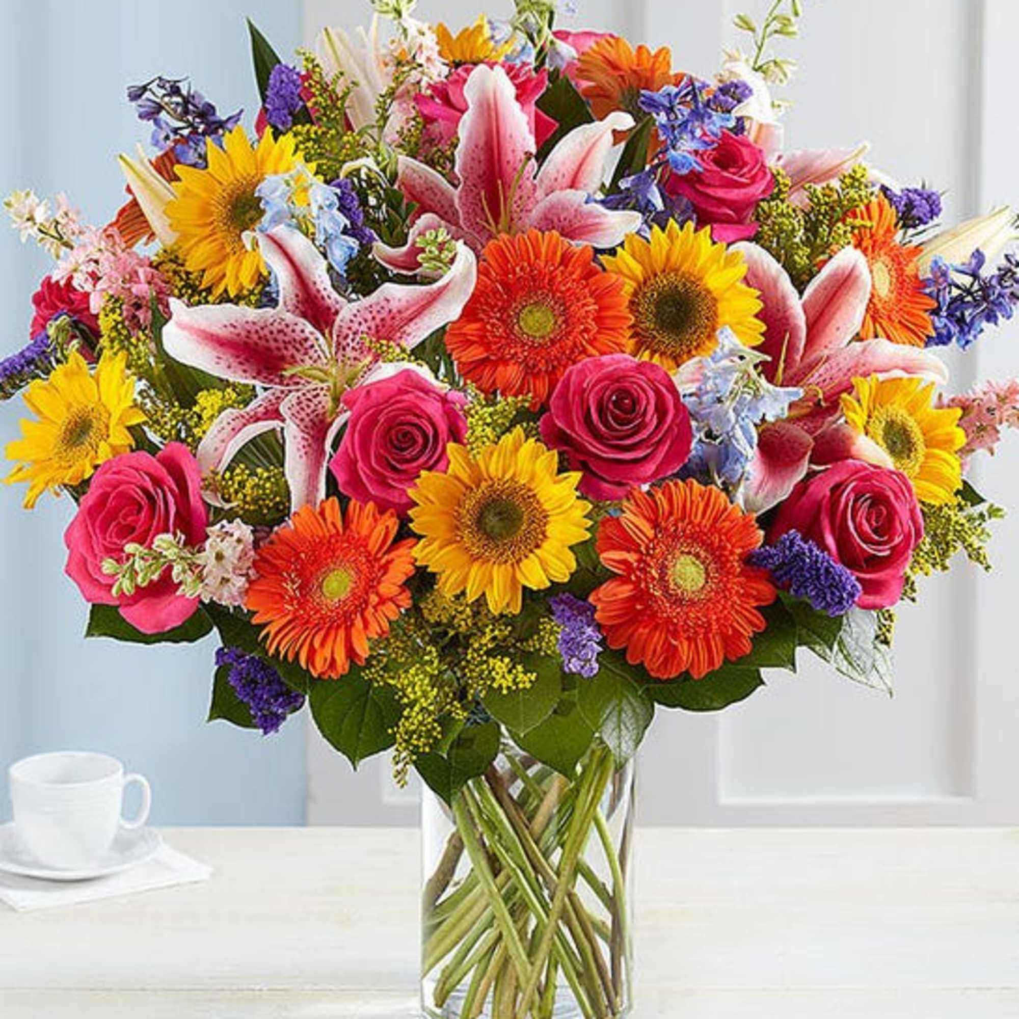 Mixed bouquet of sunflowers, roses, lilies, and gerbera daisies in a glass vase