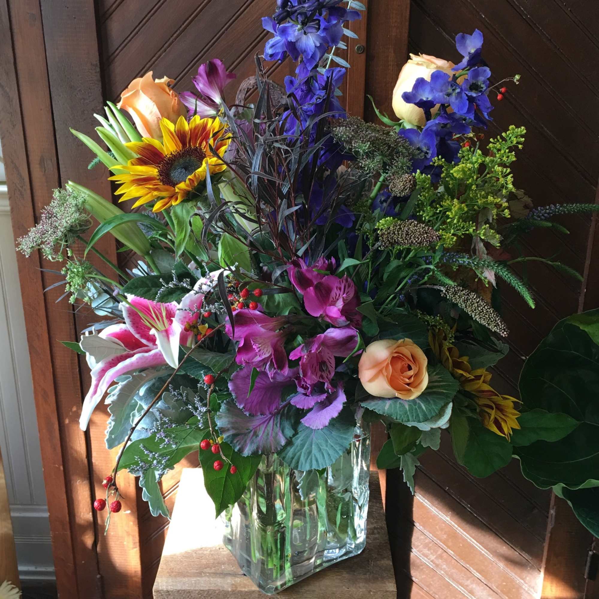 Mixed bouquet in a clear glass vase with roses, lilies, and a sunflower