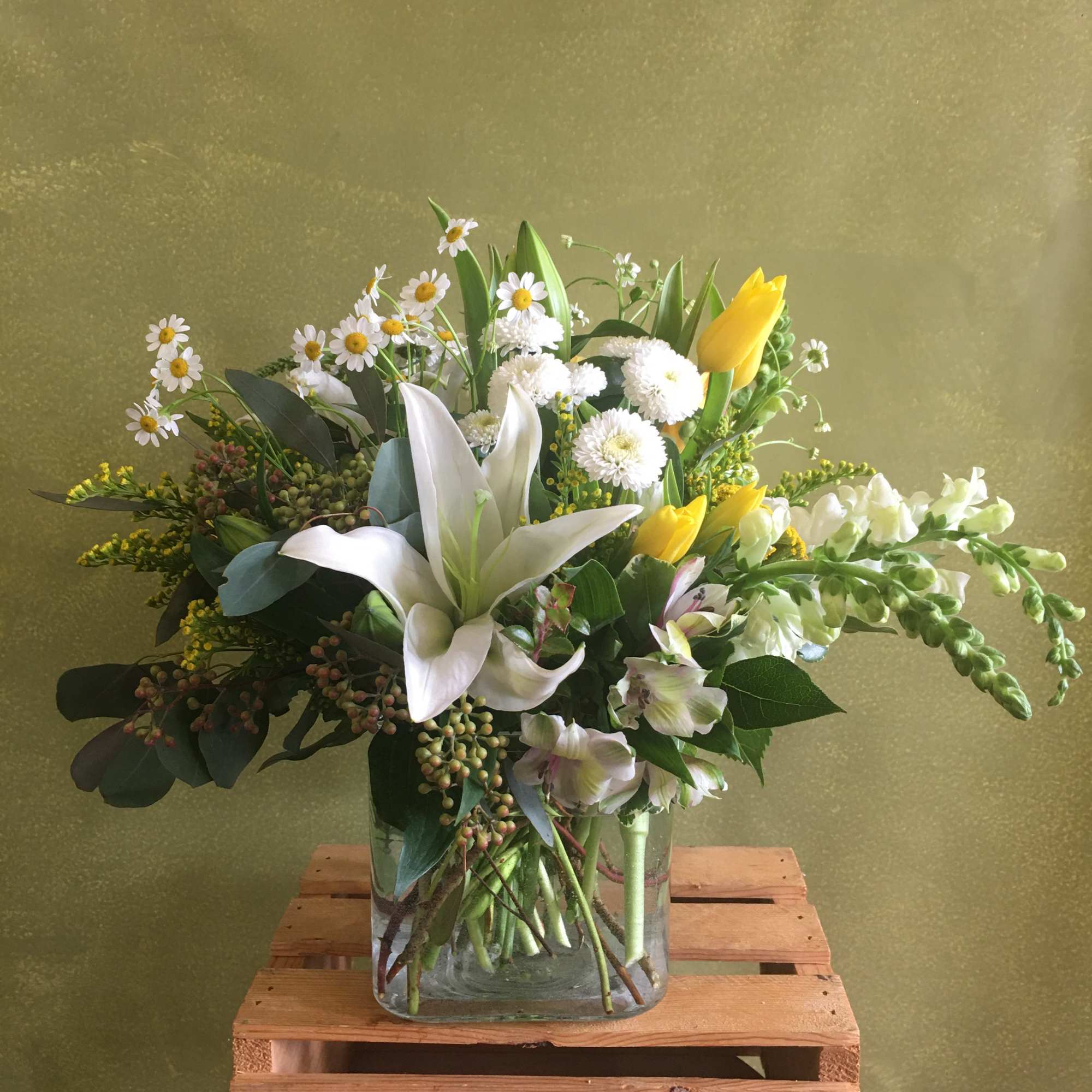 Mixed bouquet in a clear glass vase with white lilies, yellow tulips, and small white daisies