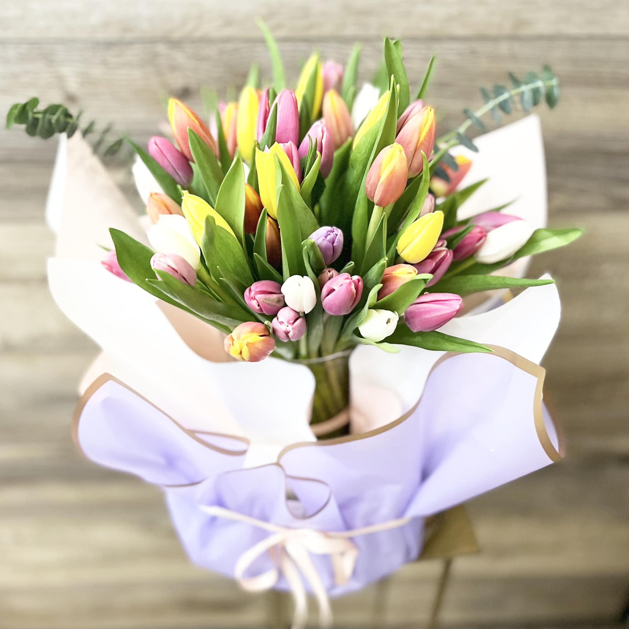Bouquet of multicolored tulips wrapped in lavender paper