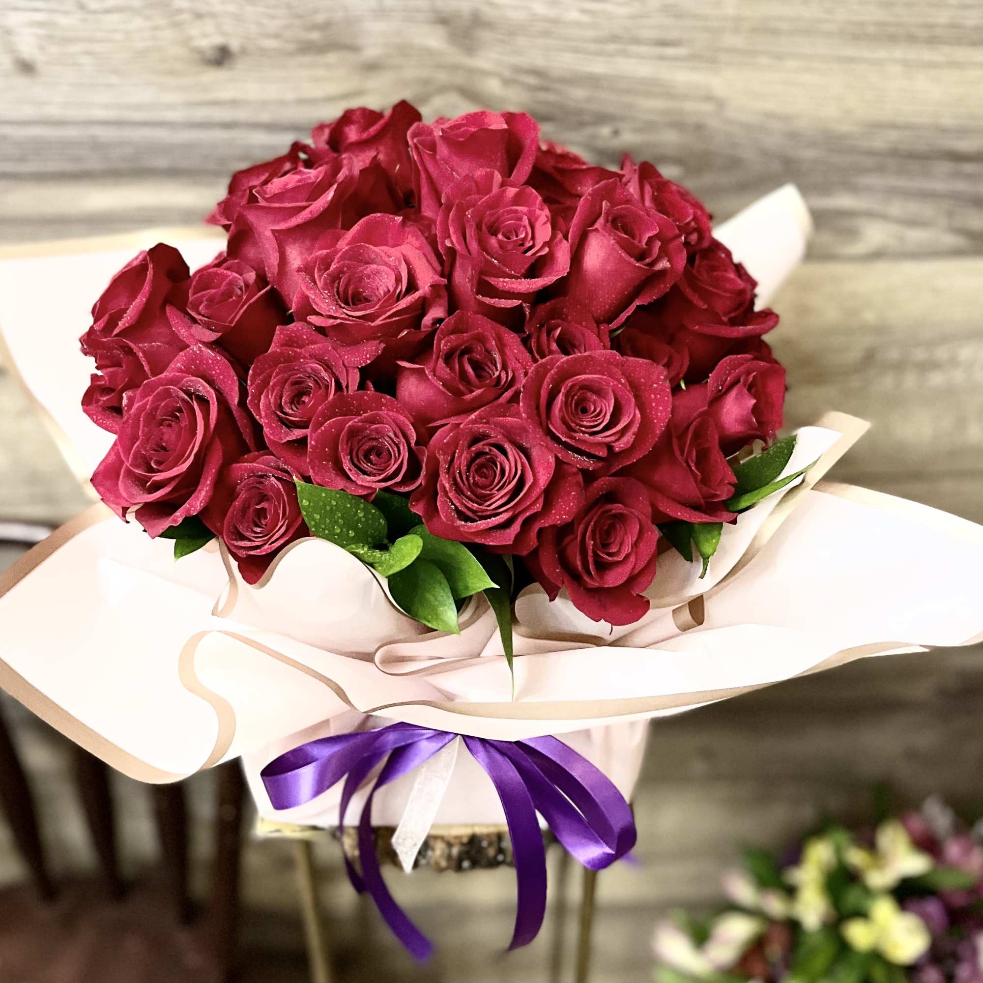 Bouquet of deep pink roses wrapped in pale paper with a purple ribbon