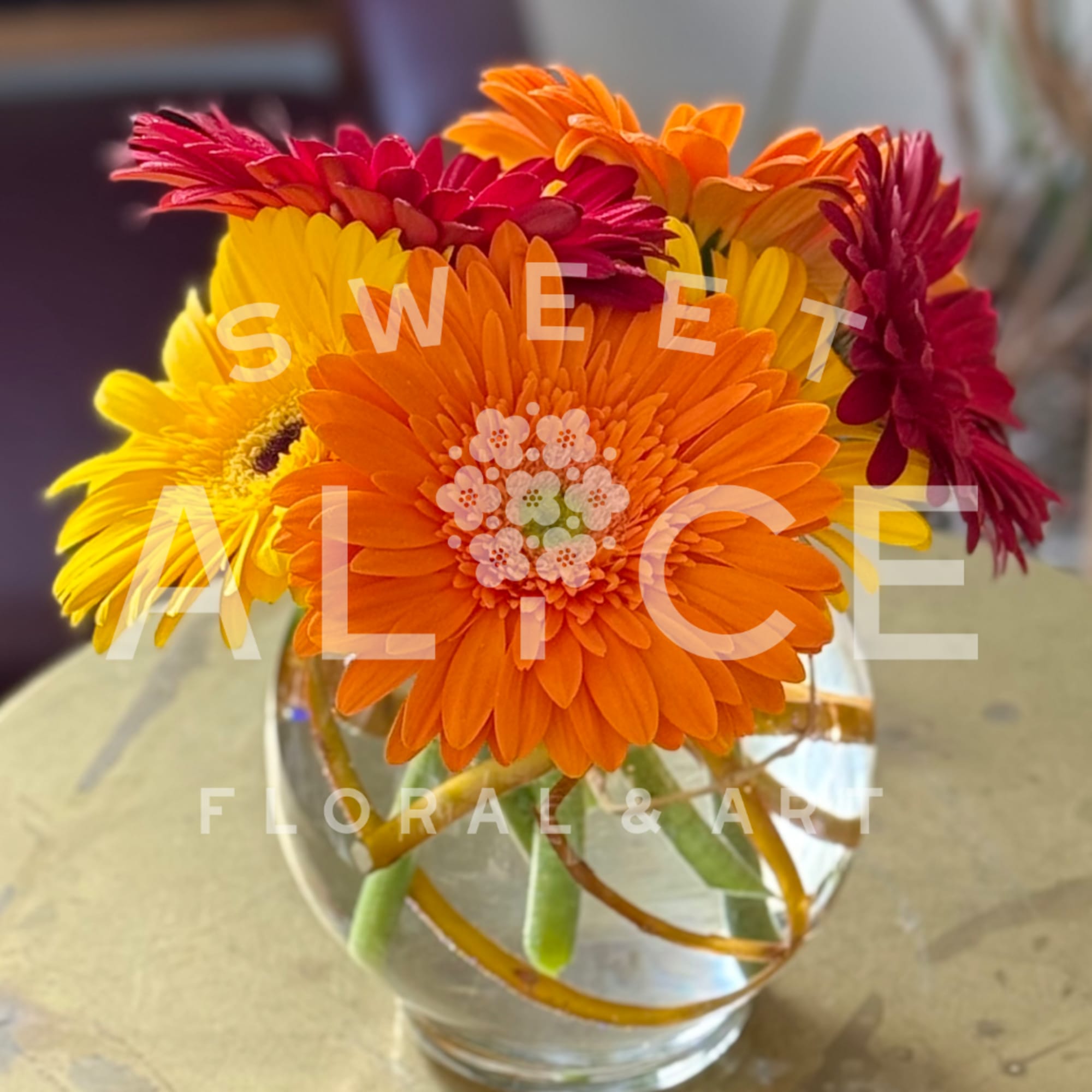 Bright gerbera daisies in orange, yellow, and red arranged in a glass vase