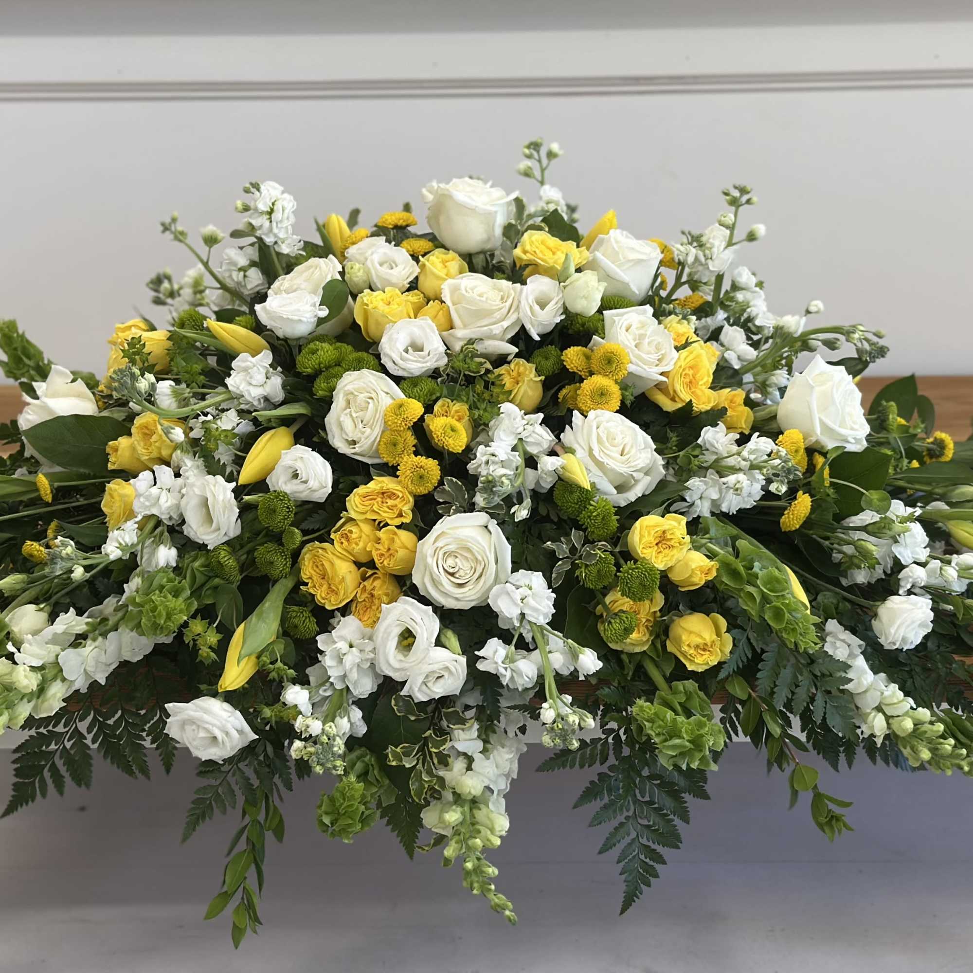 Large white and yellow floral casket spray on a wooden table