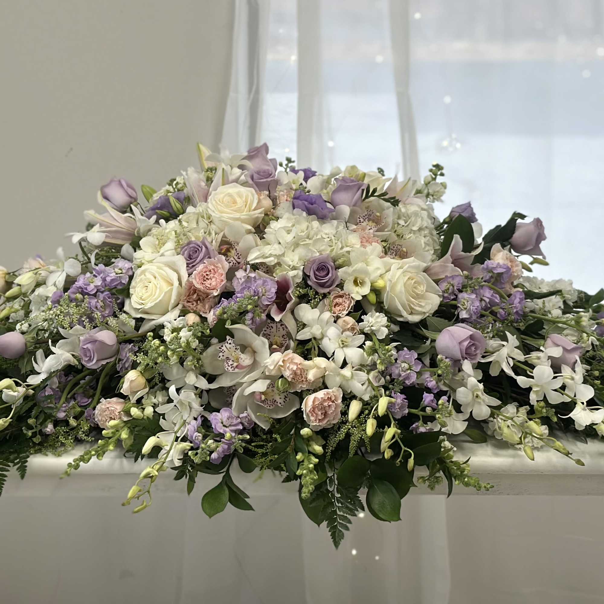 Large pastel floral casket spray with roses, orchids, and hydrangeas