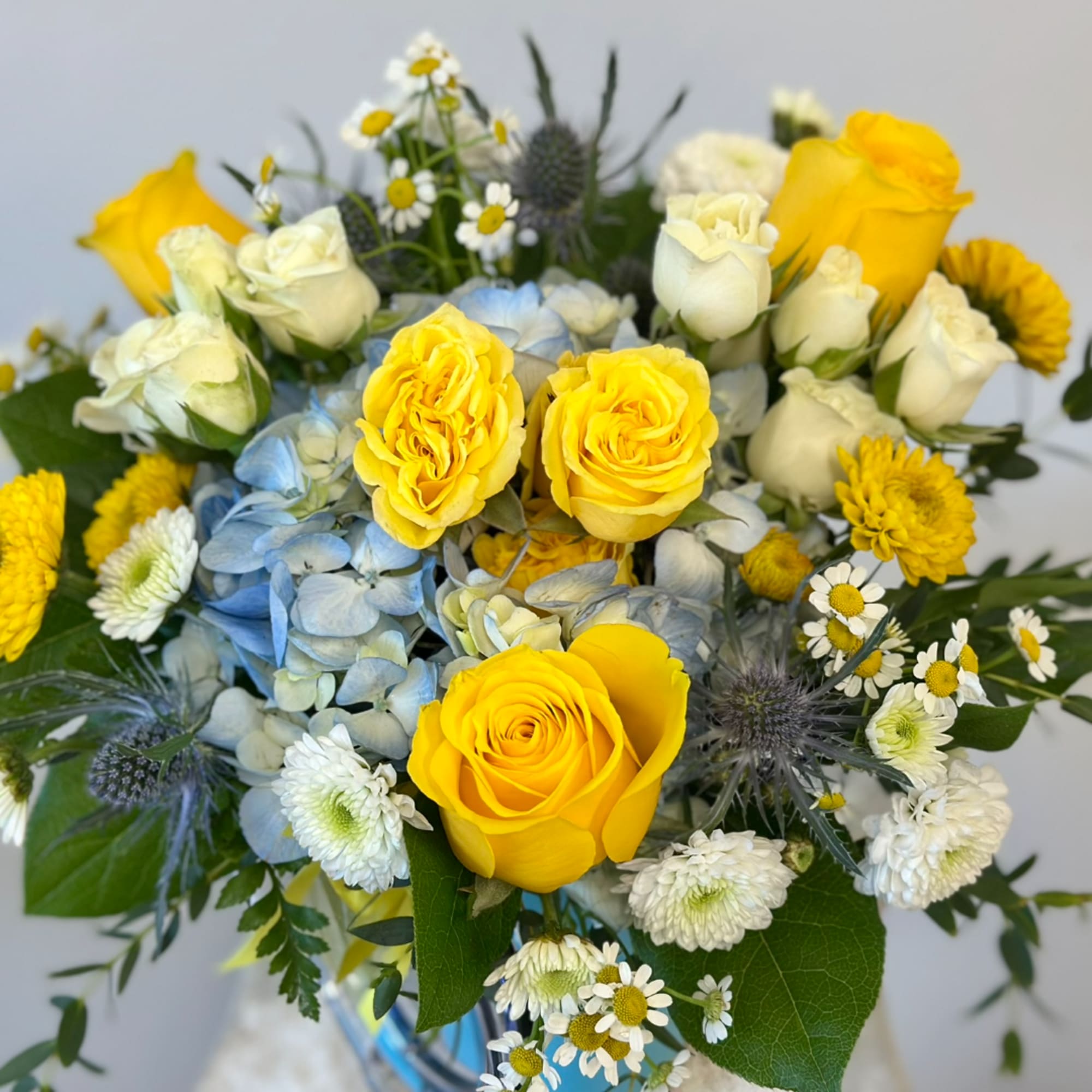 Yellow and white roses with blue hydrangea and small daisy flowers in a vase