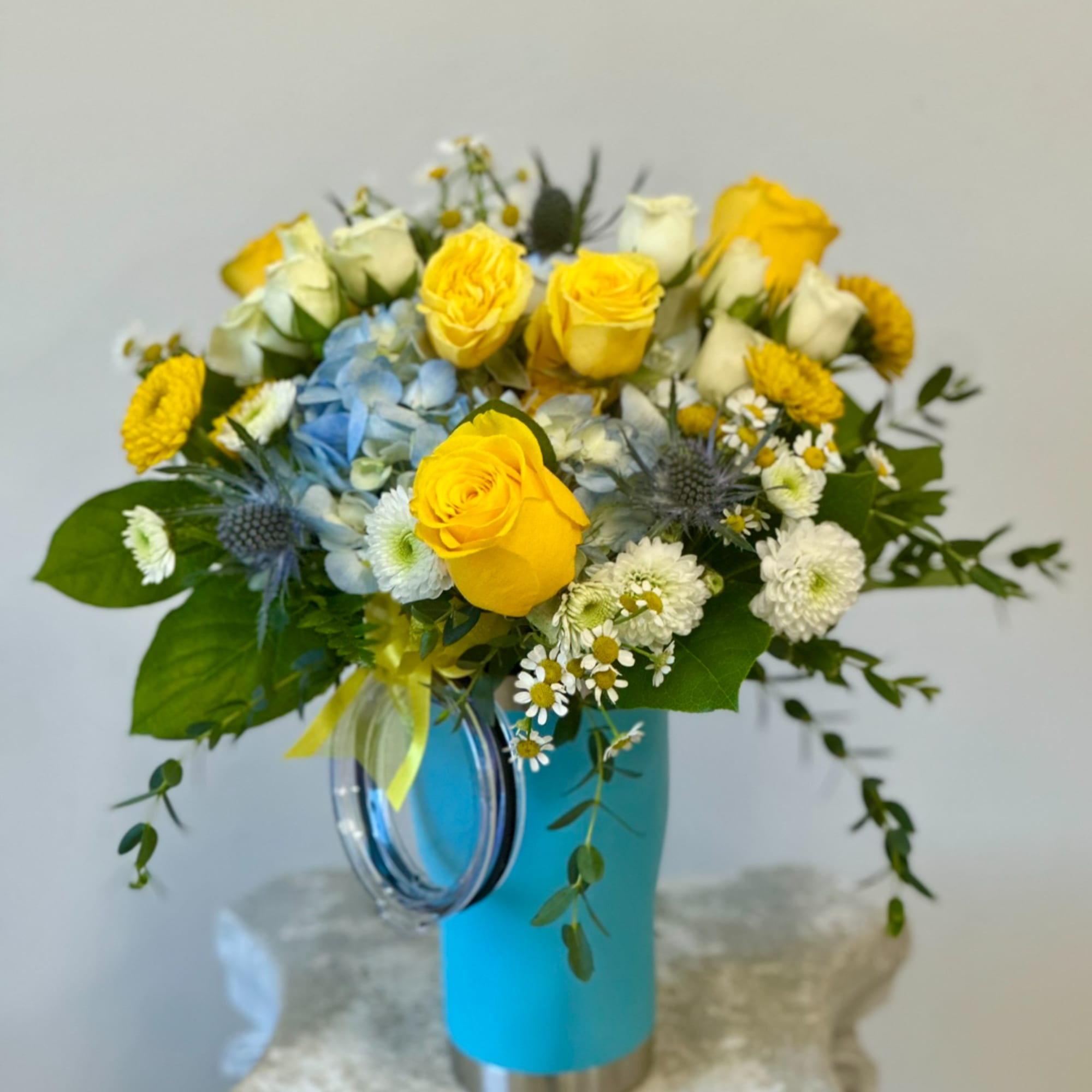 Yellow roses and mixed white flowers in a blue vase with a ribbon