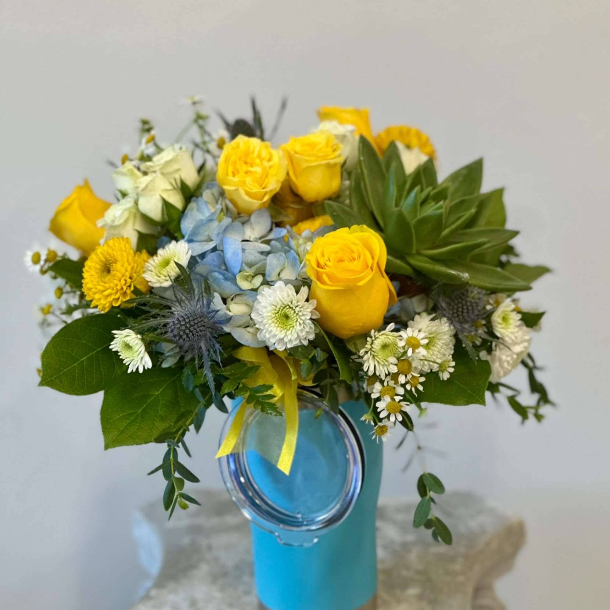 Yellow roses and mixed blooms in a blue vase with a yellow ribbon