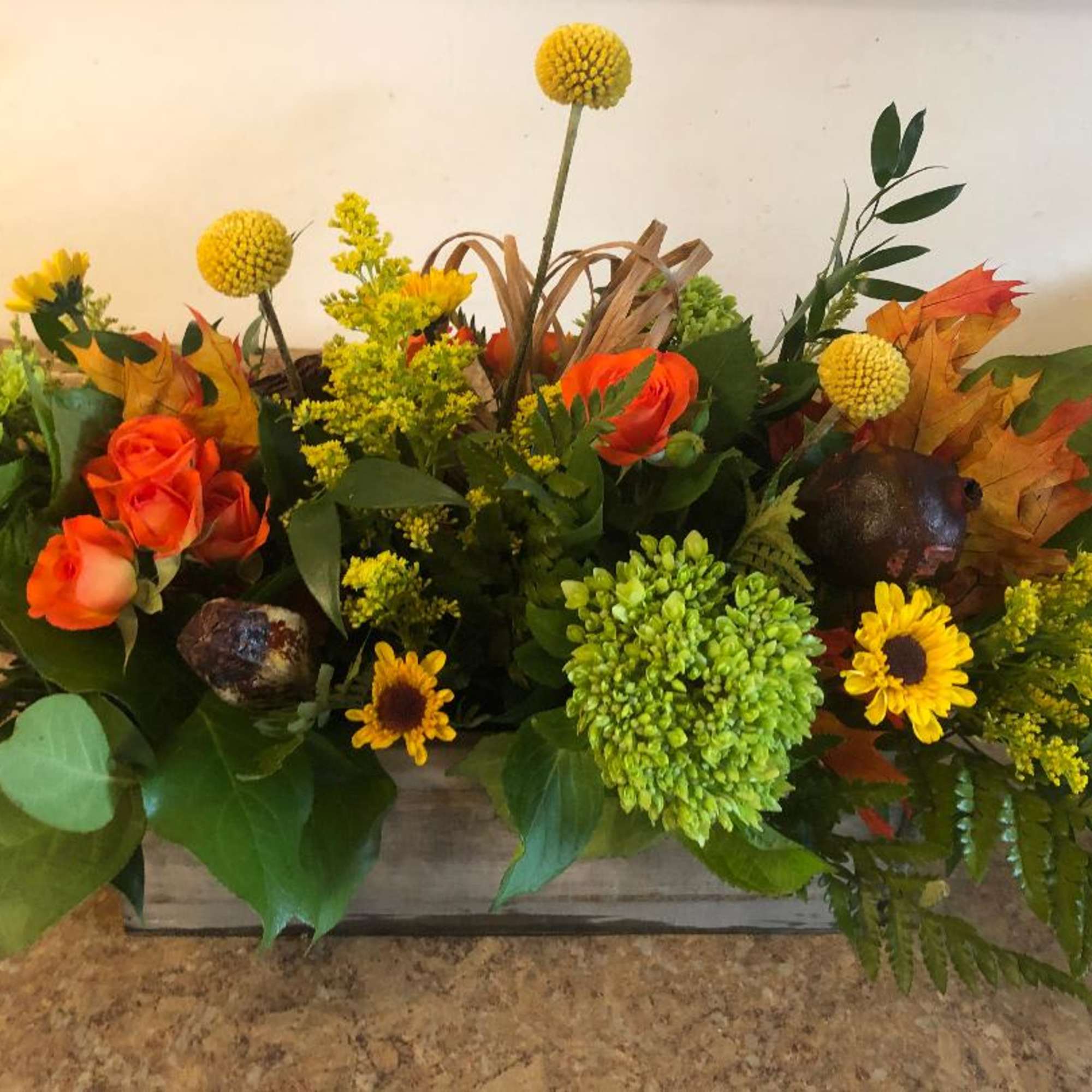 Orange roses and yellow flowers arranged in a low wooden box