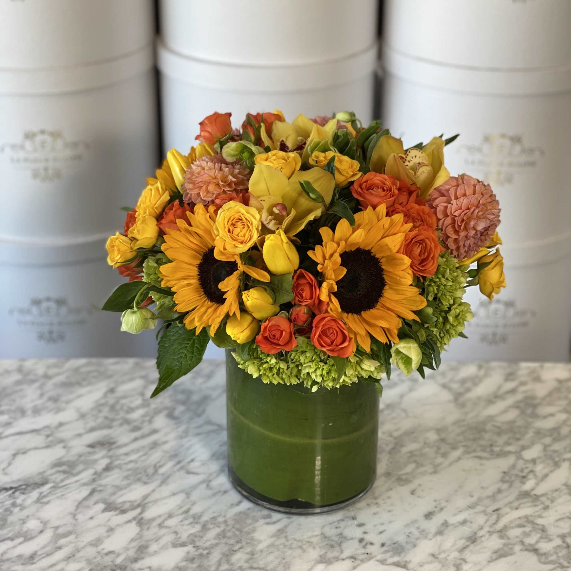 Bouquet of sunflowers, yellow roses, and orange blooms in a green vase