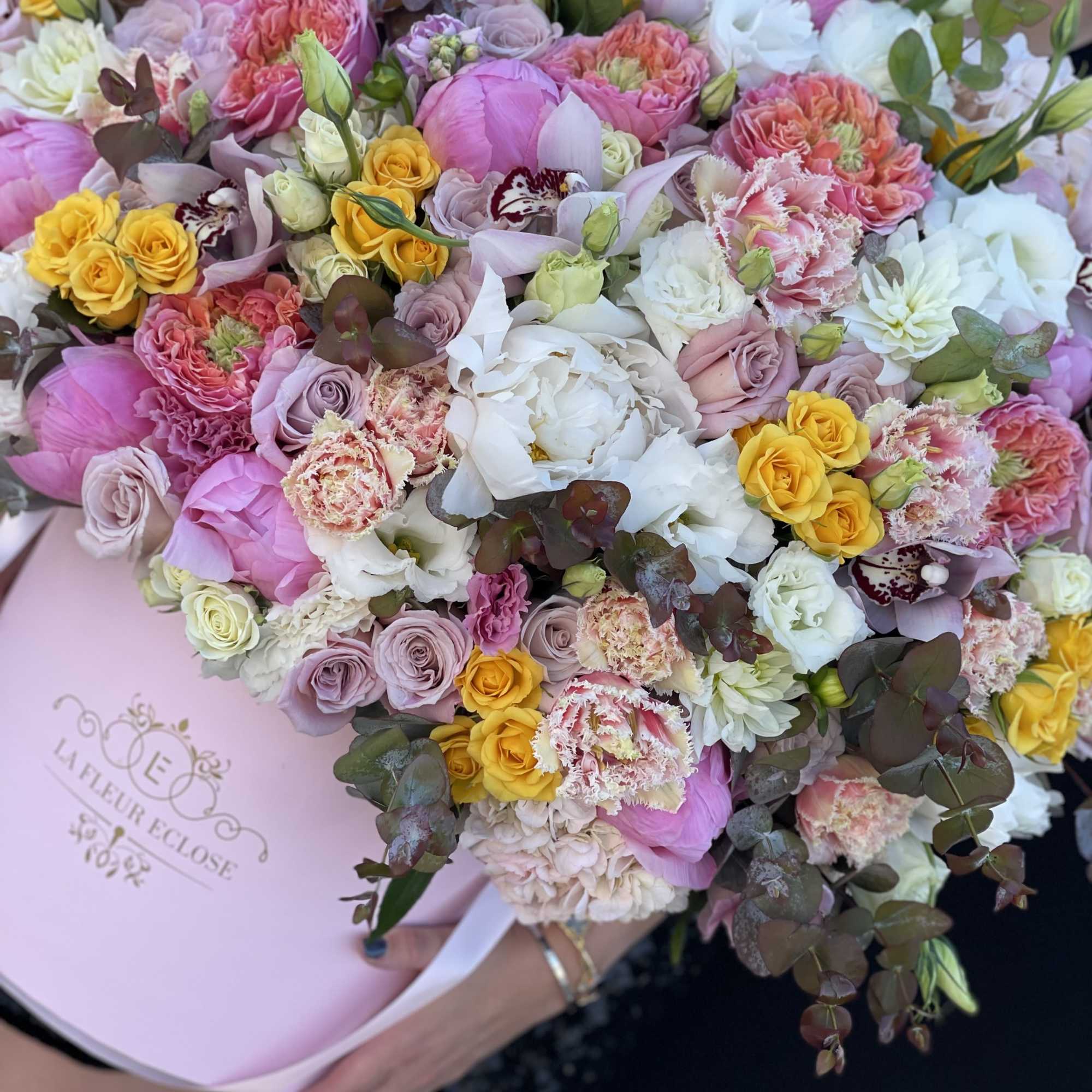 Large pastel bouquet of roses, peonies, and orchids in pink wrapping