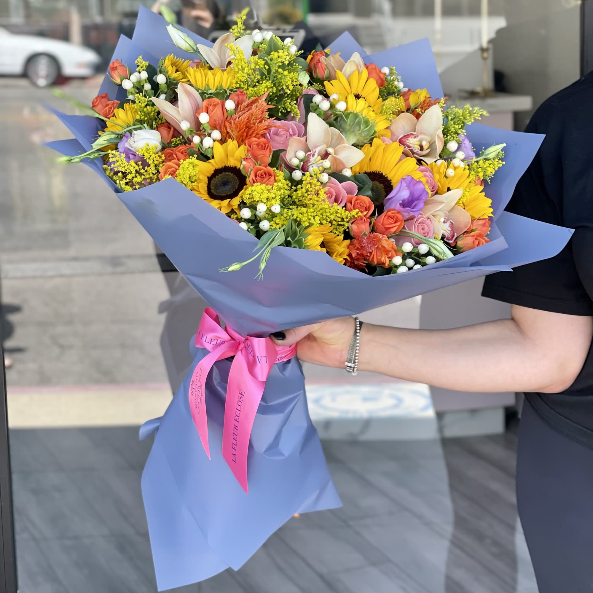 Large mixed bouquet with sunflowers, roses, and orchids wrapped in blue paper