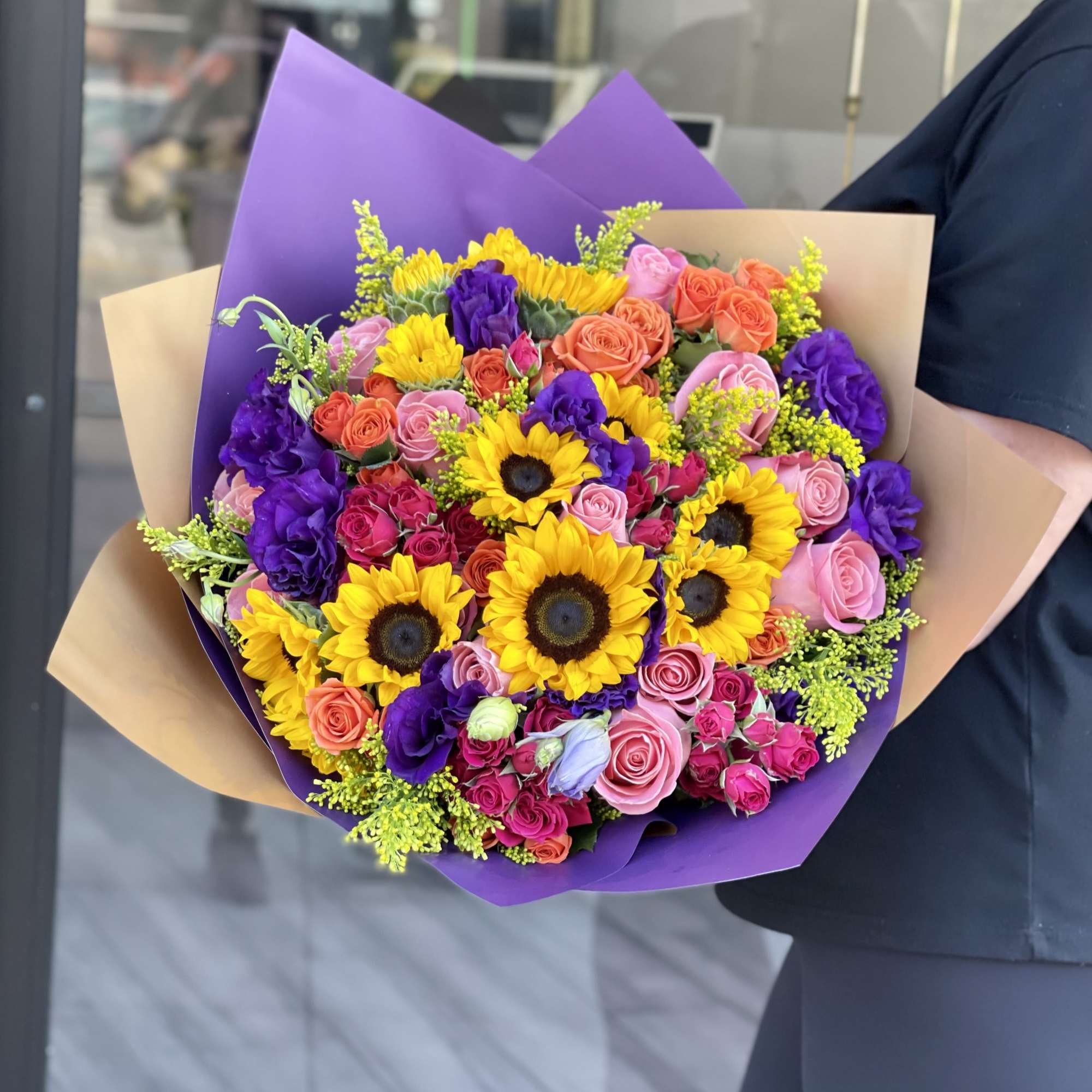 Large bouquet of sunflowers and multicolored roses wrapped in purple and tan paper