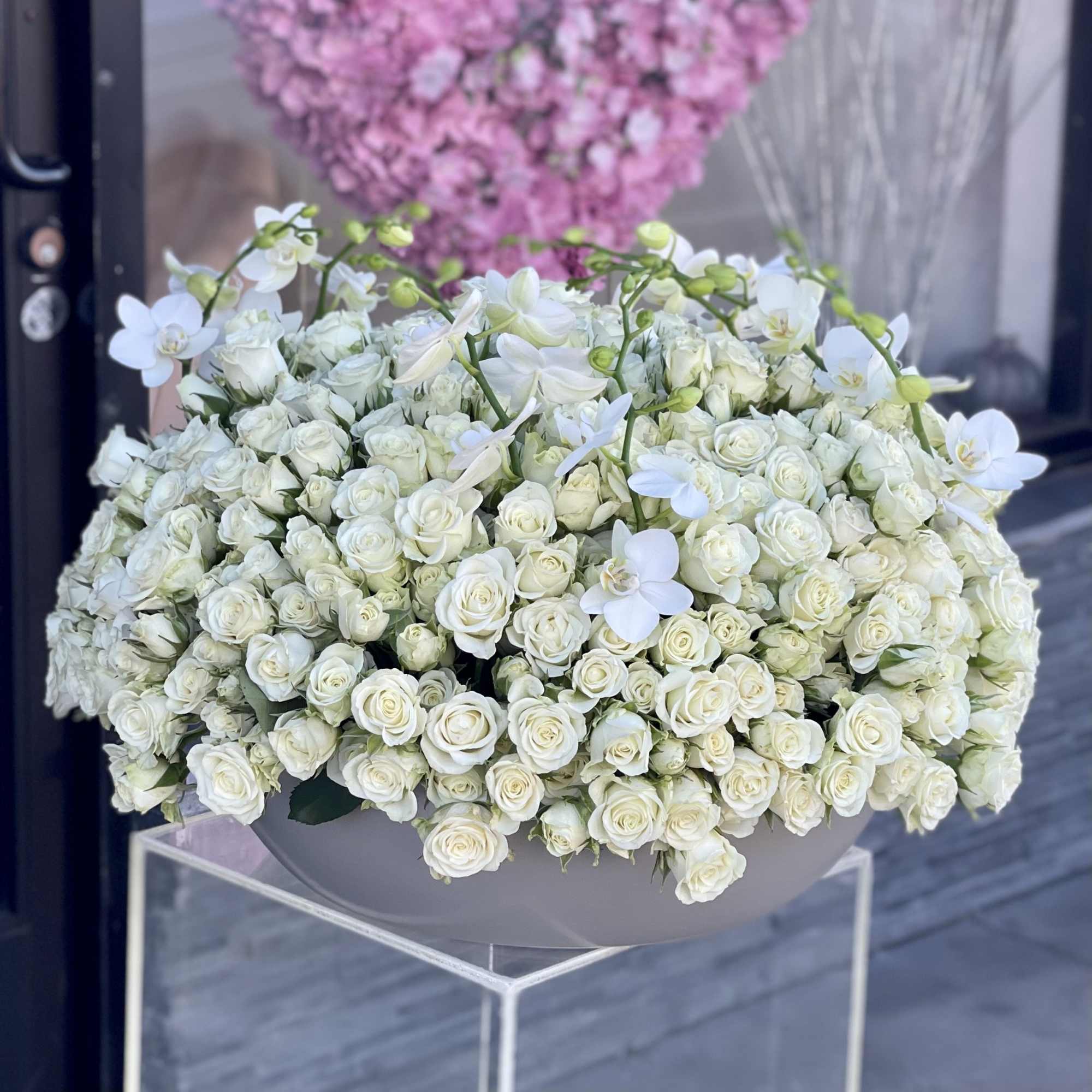 Large white rose arrangement with white orchids in a gray container
