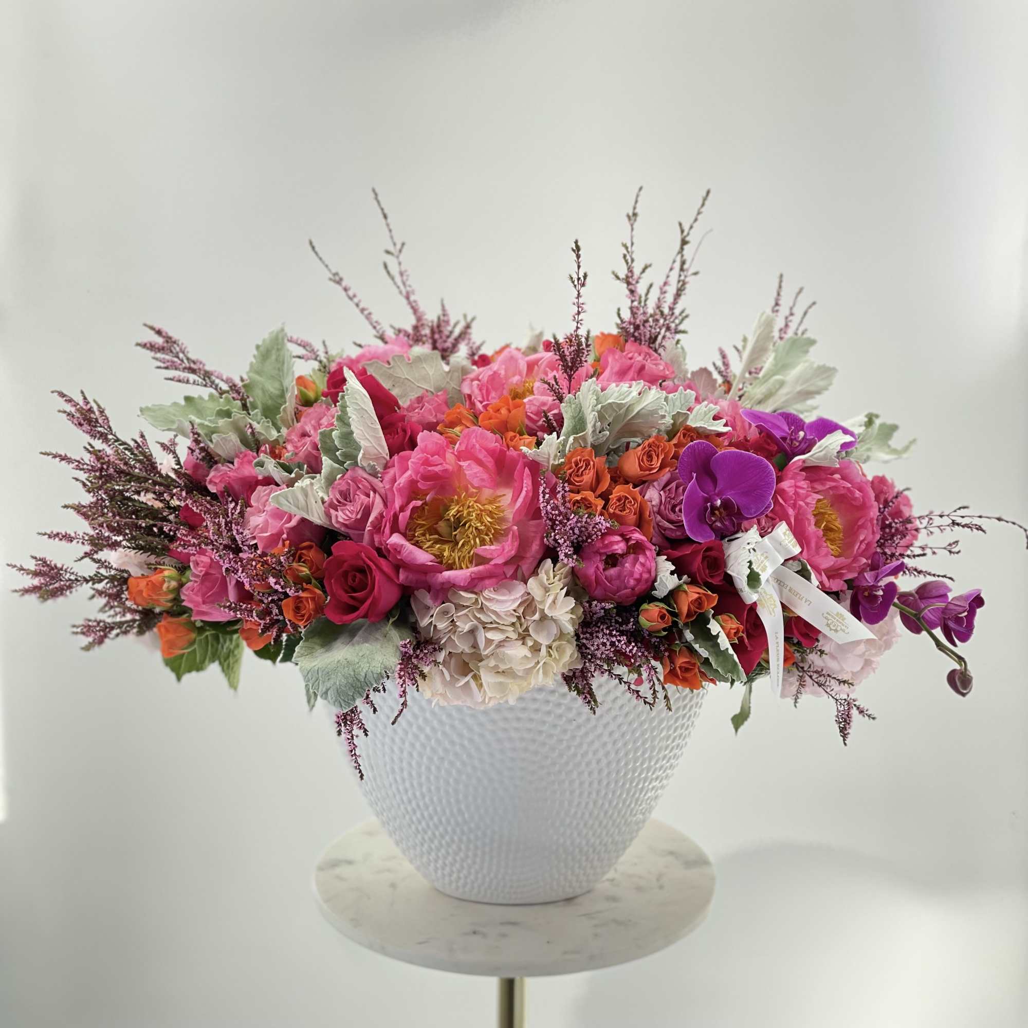 Bright pink and purple floral arrangement in a white textured vase
