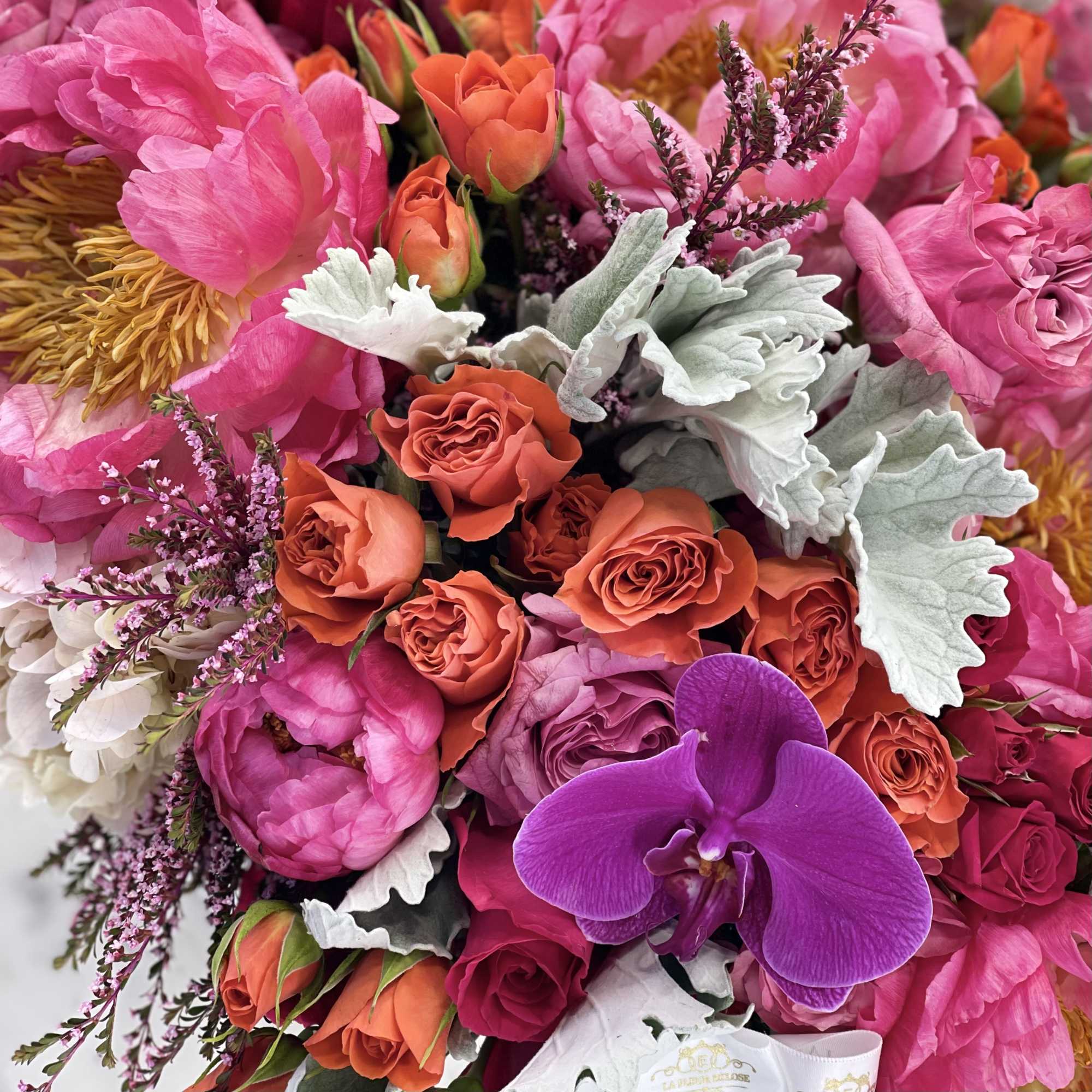 Bouquet of pink and orange flowers with a purple orchid and silver foliage