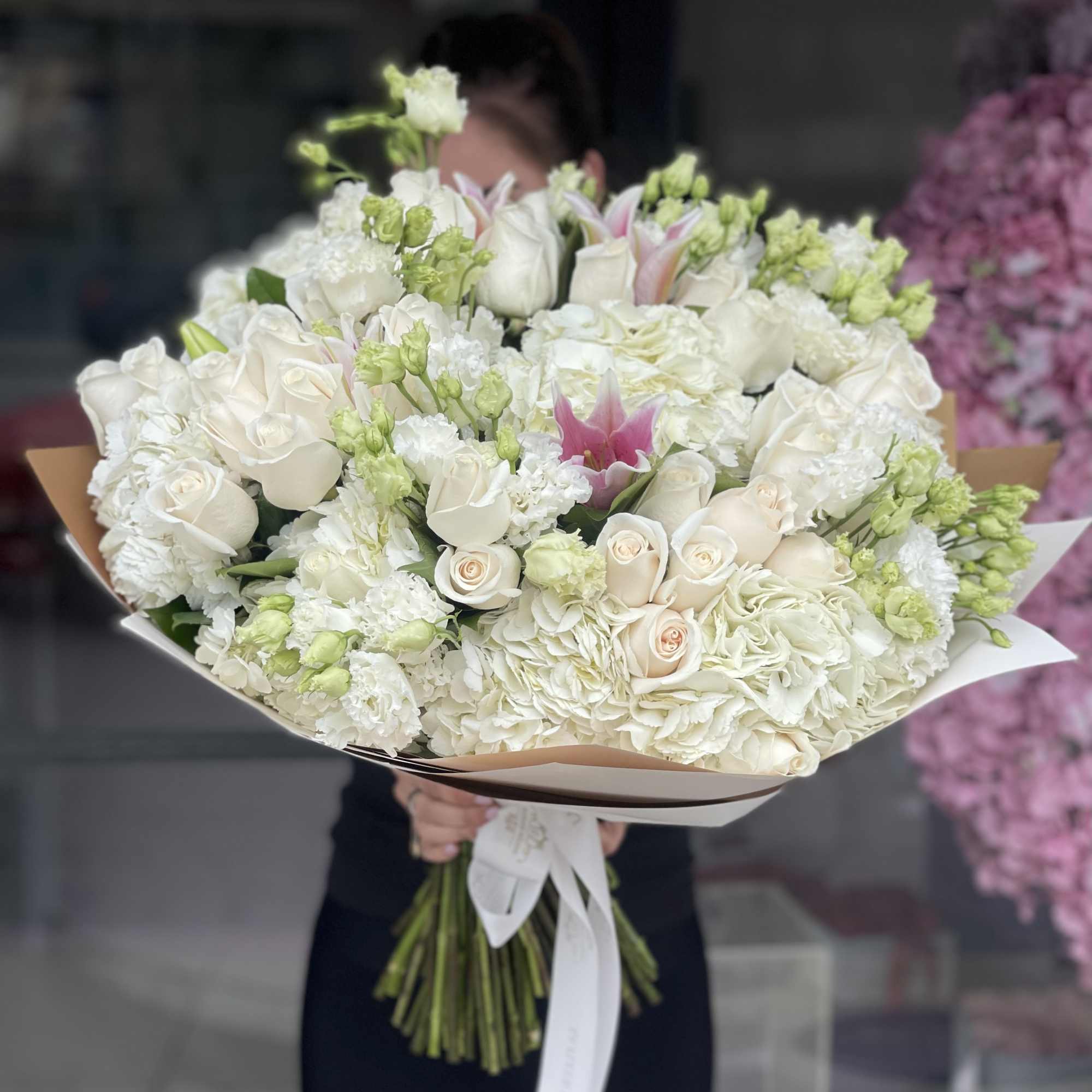 Large bouquet of white roses and lilies wrapped in paper with a ribbon