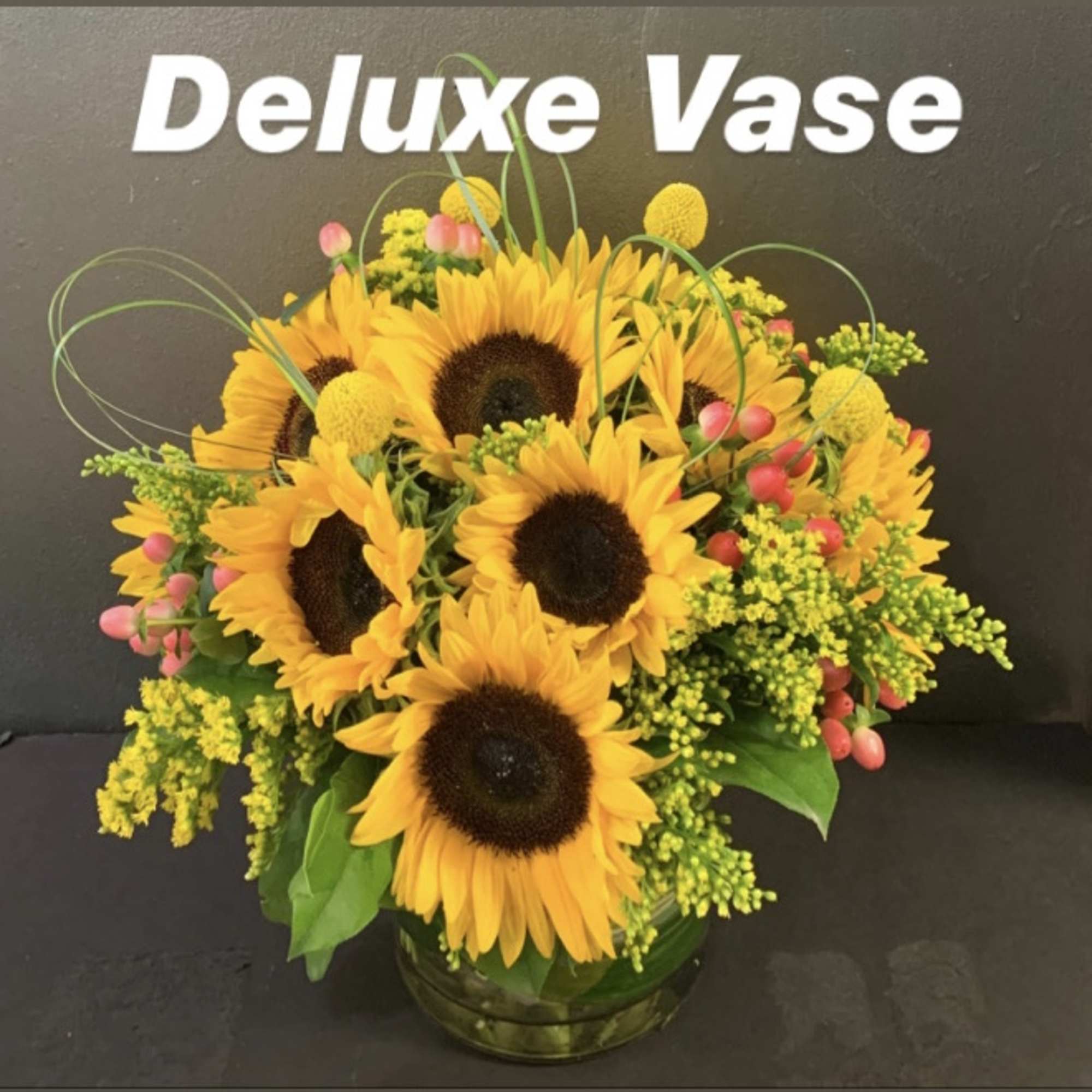 Bouquet of sunflowers in a glass vase with yellow filler flowers and pink berries.